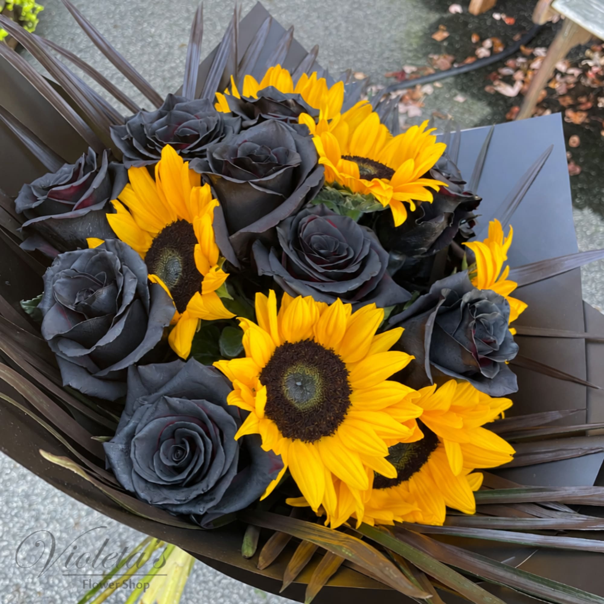 Bouquet of black roses and bright yellow sunflowers wrapped in dark paper