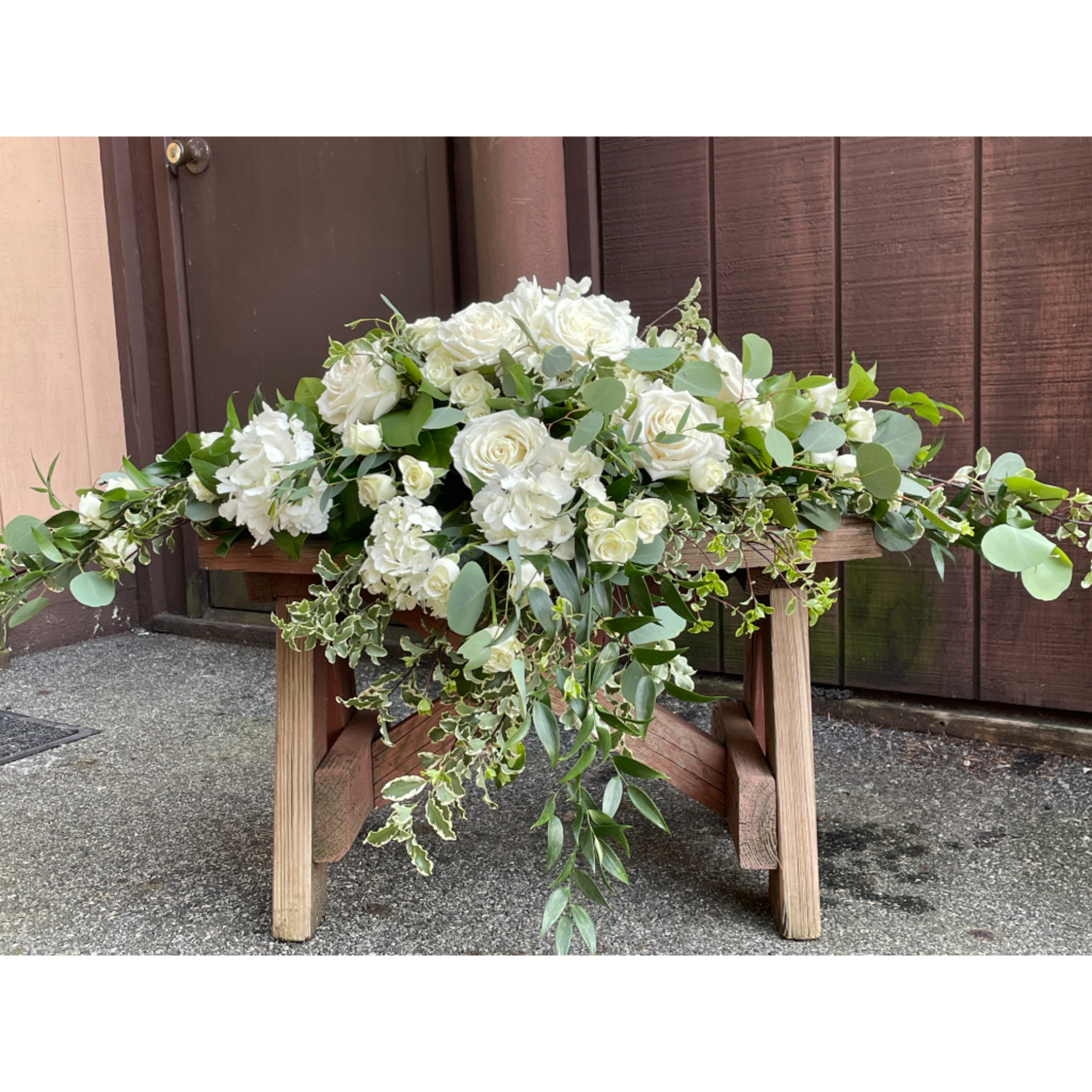 White roses and hydrangeas arranged on a wooden table with trailing greenery