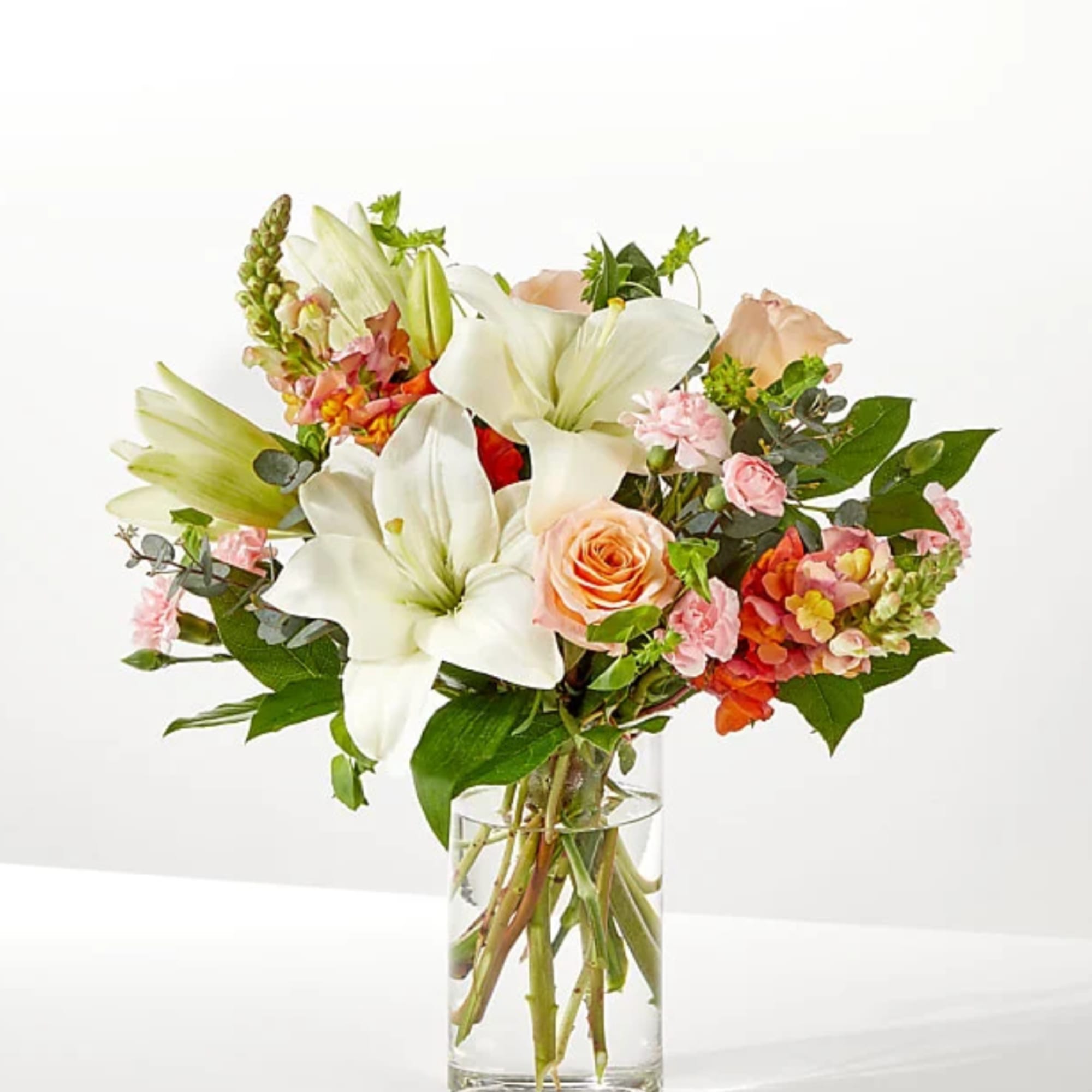 Bouquet of white lilies, peach roses, and pink flowers in a clear glass vase