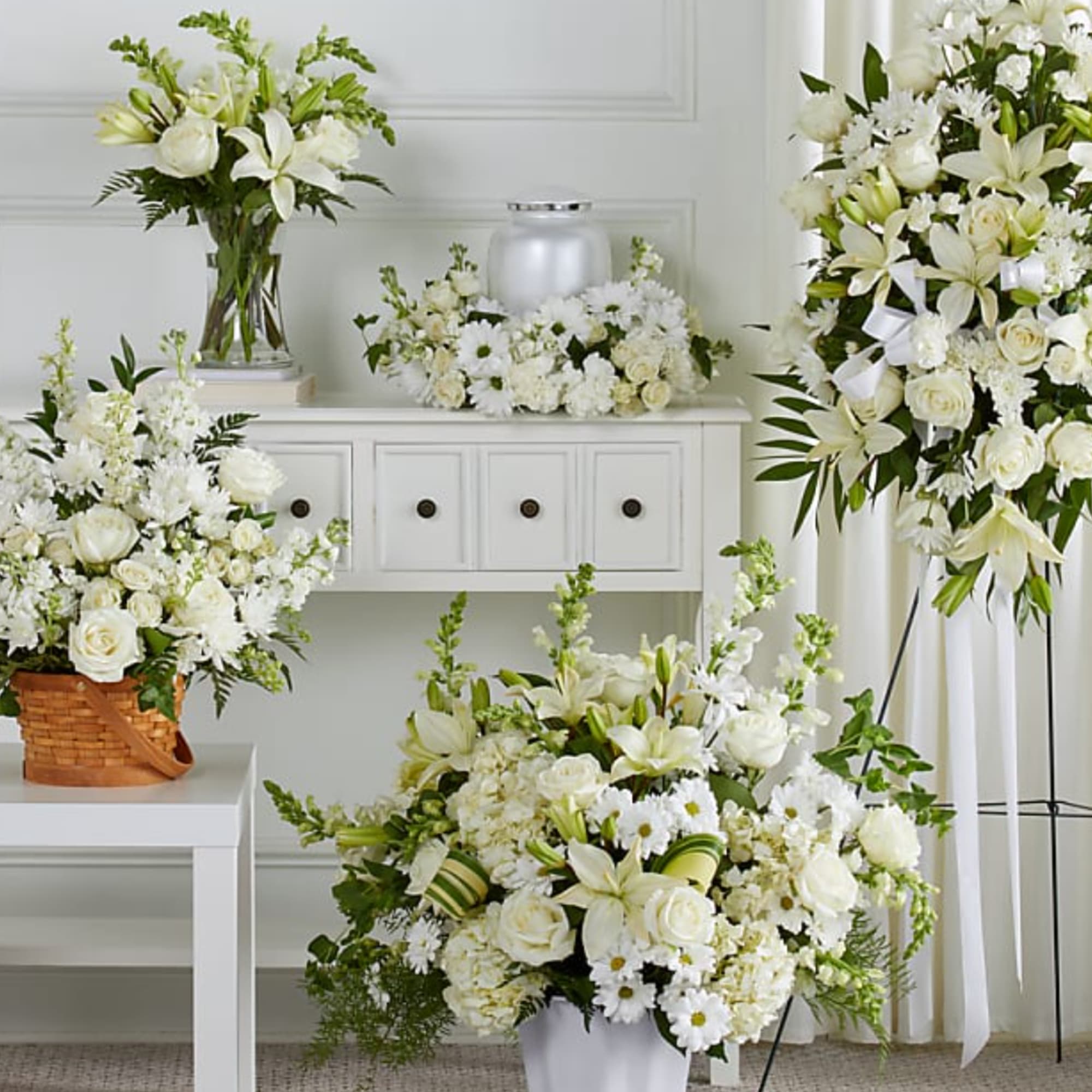 White floral arrangements with lilies and roses in vases and a standing spray