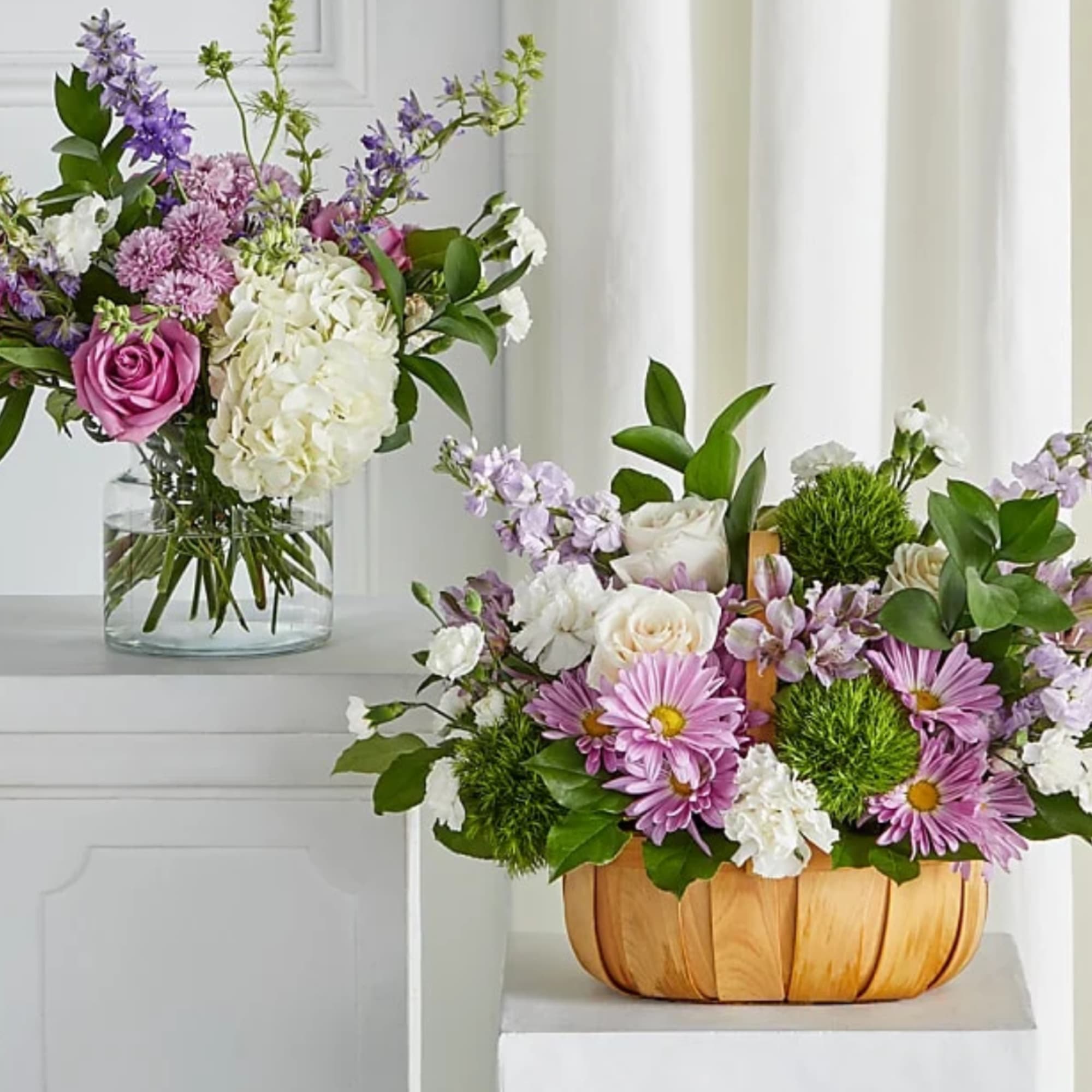 Two floral arrangements with pink, white, and purple blooms, one in a glass vase and one in a wooden basket