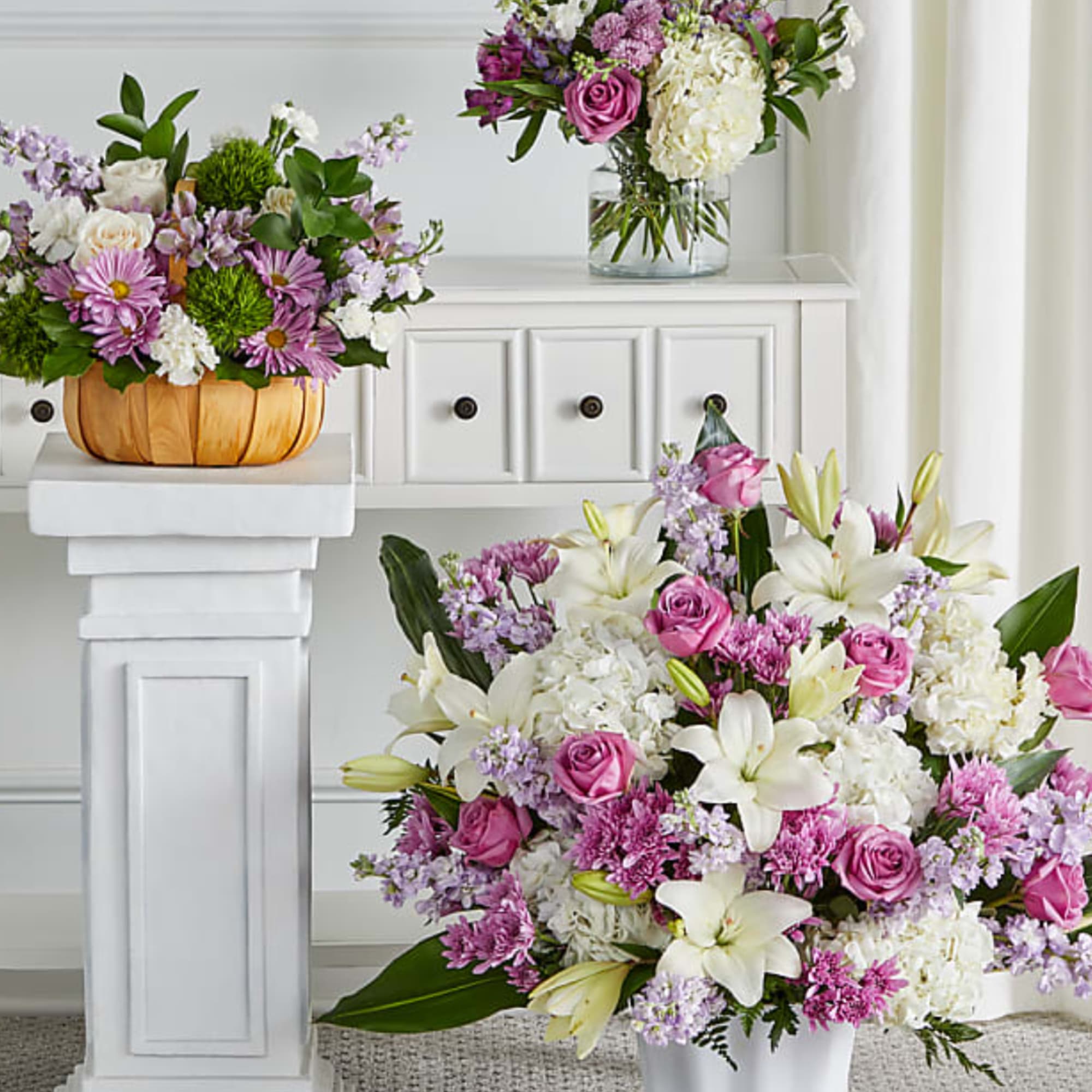Three floral arrangements with pink, white, and lavender blooms in vases and a basket