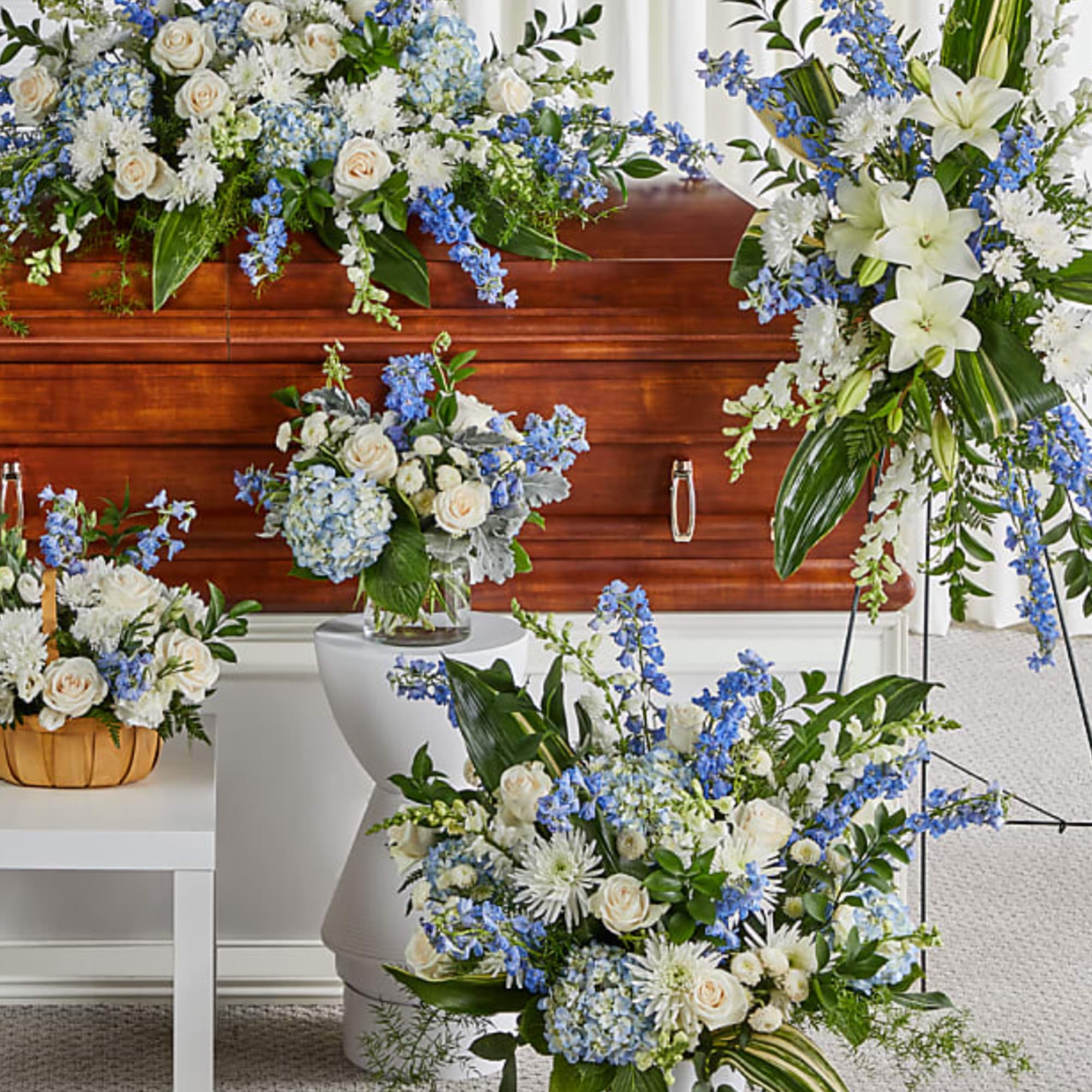 White and blue floral funeral arrangements displayed around a wooden casket