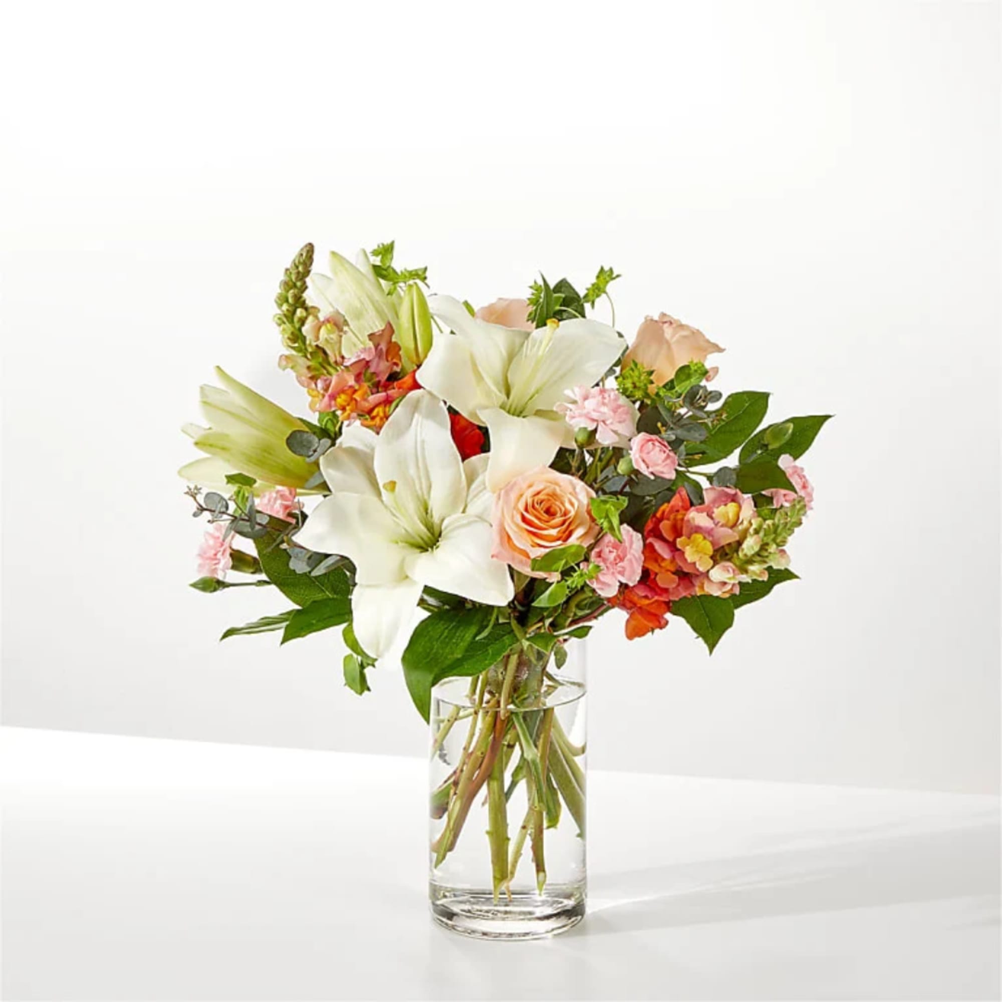 White lilies and peach roses in a clear glass vase