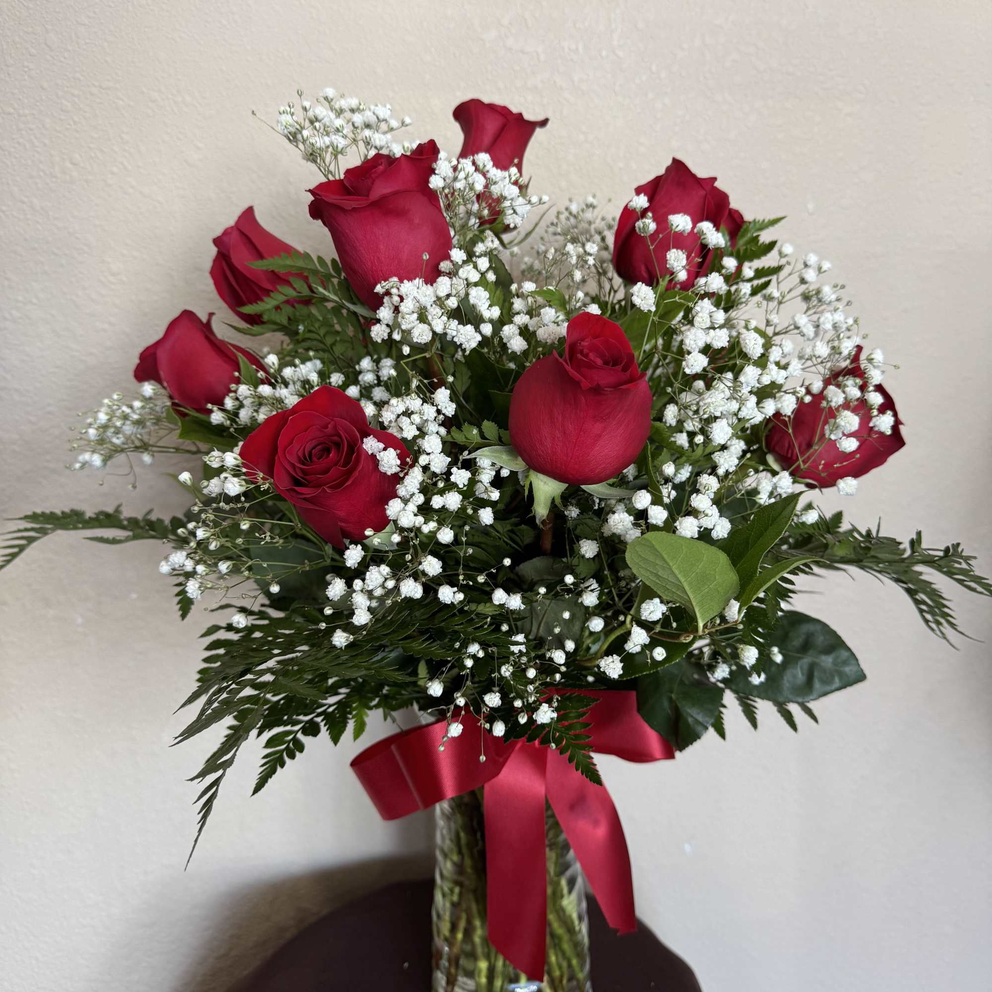 Red roses with white baby's breath in a glass vase tied with a red ribbon