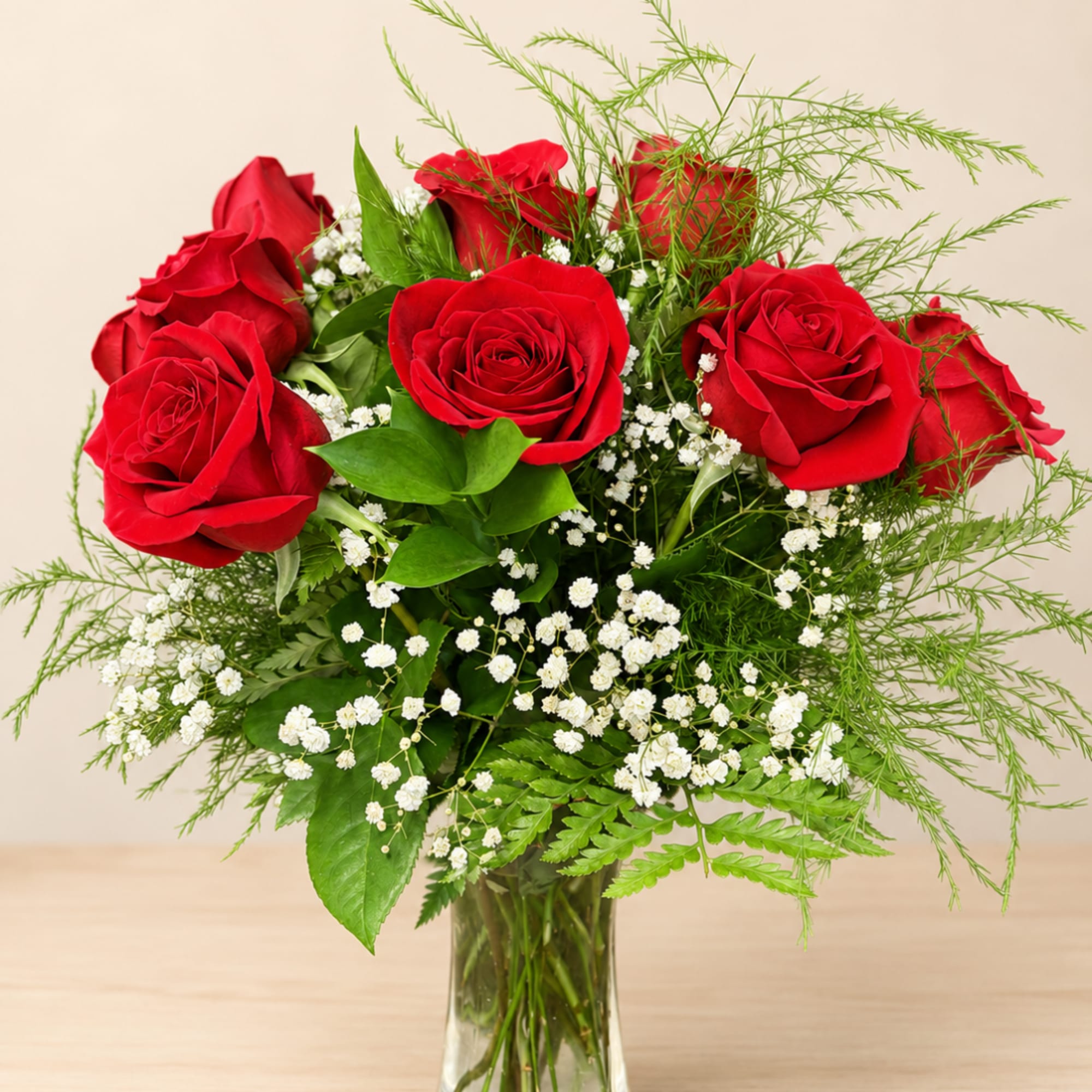 Red roses arranged in a clear glass vase with white filler flowers