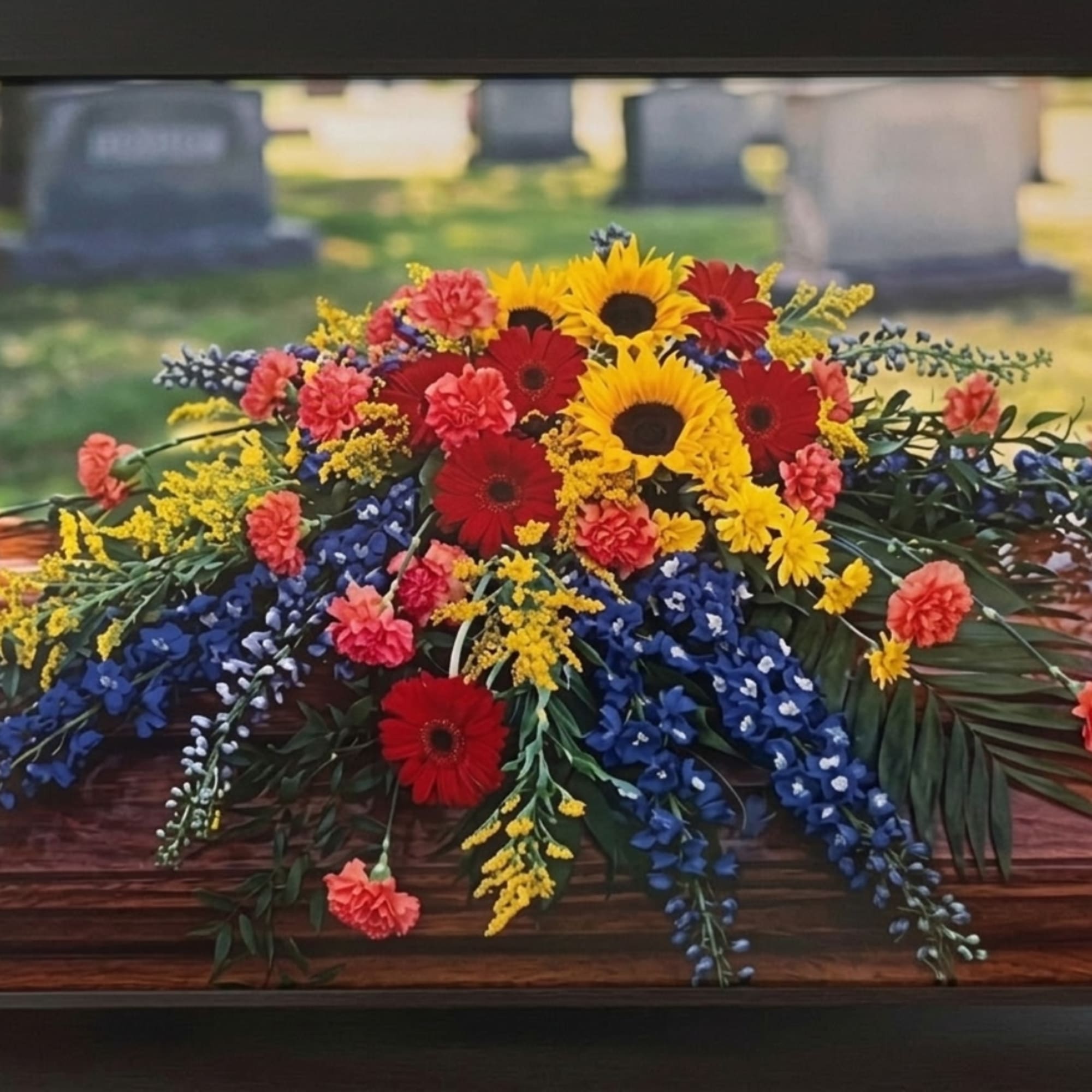 Colorful floral casket spray with sunflowers, red gerberas, and blue flowers