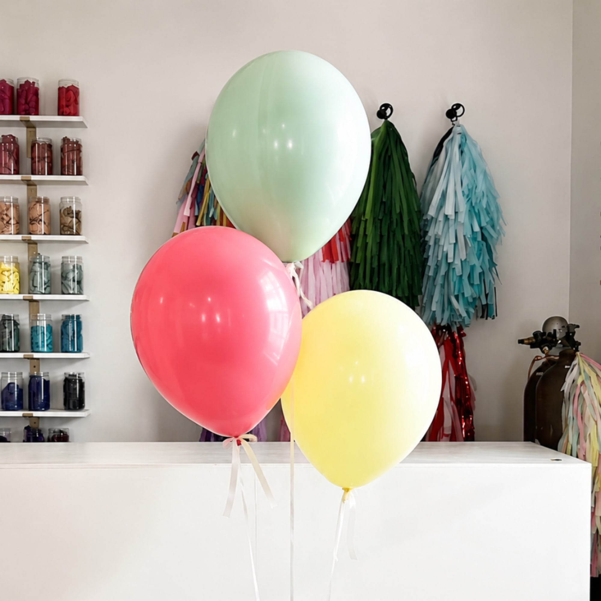 Three pastel balloons in a shop interior, with ribbon tails.