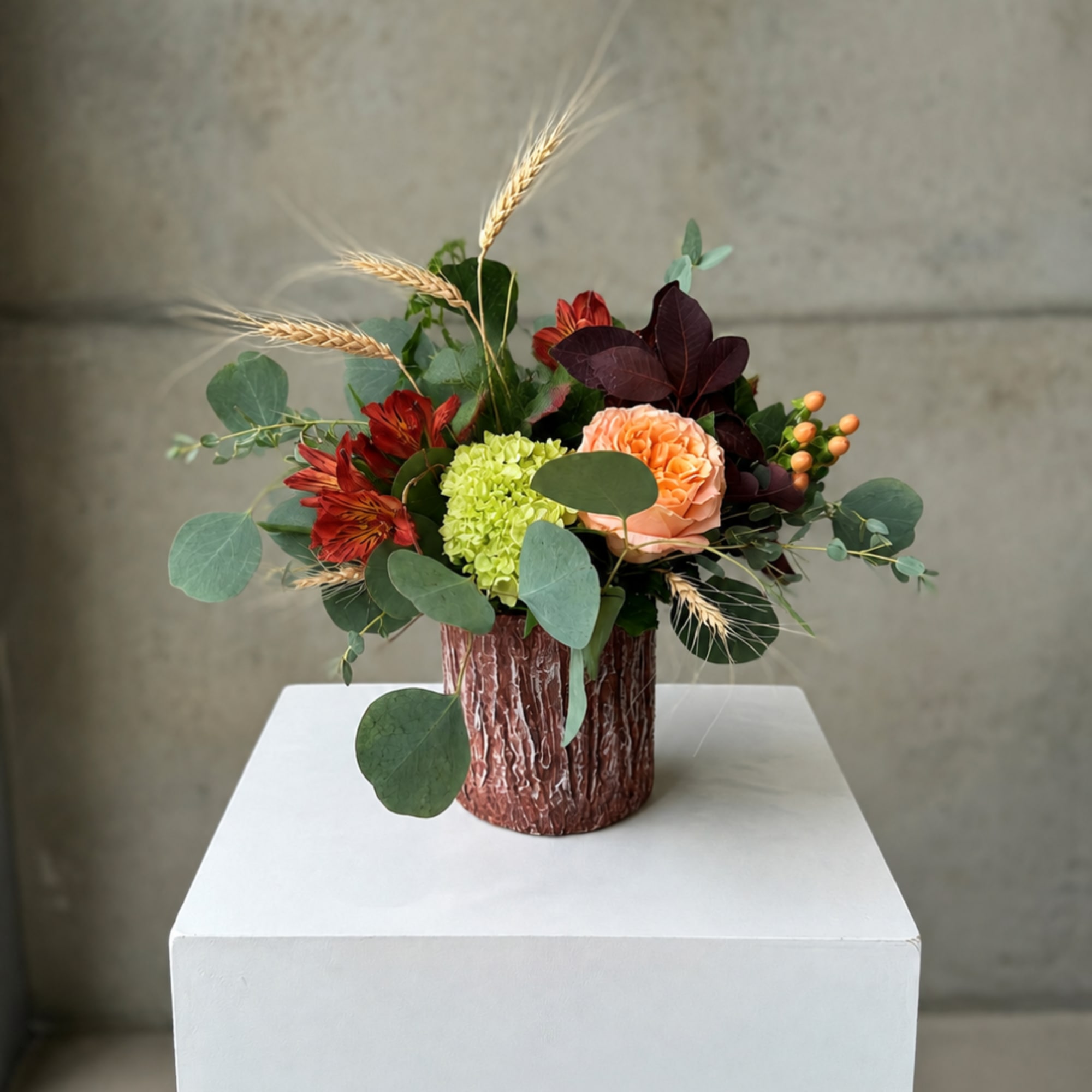 Mixed bouquet in a textured brown vase with peach, red, and green blooms