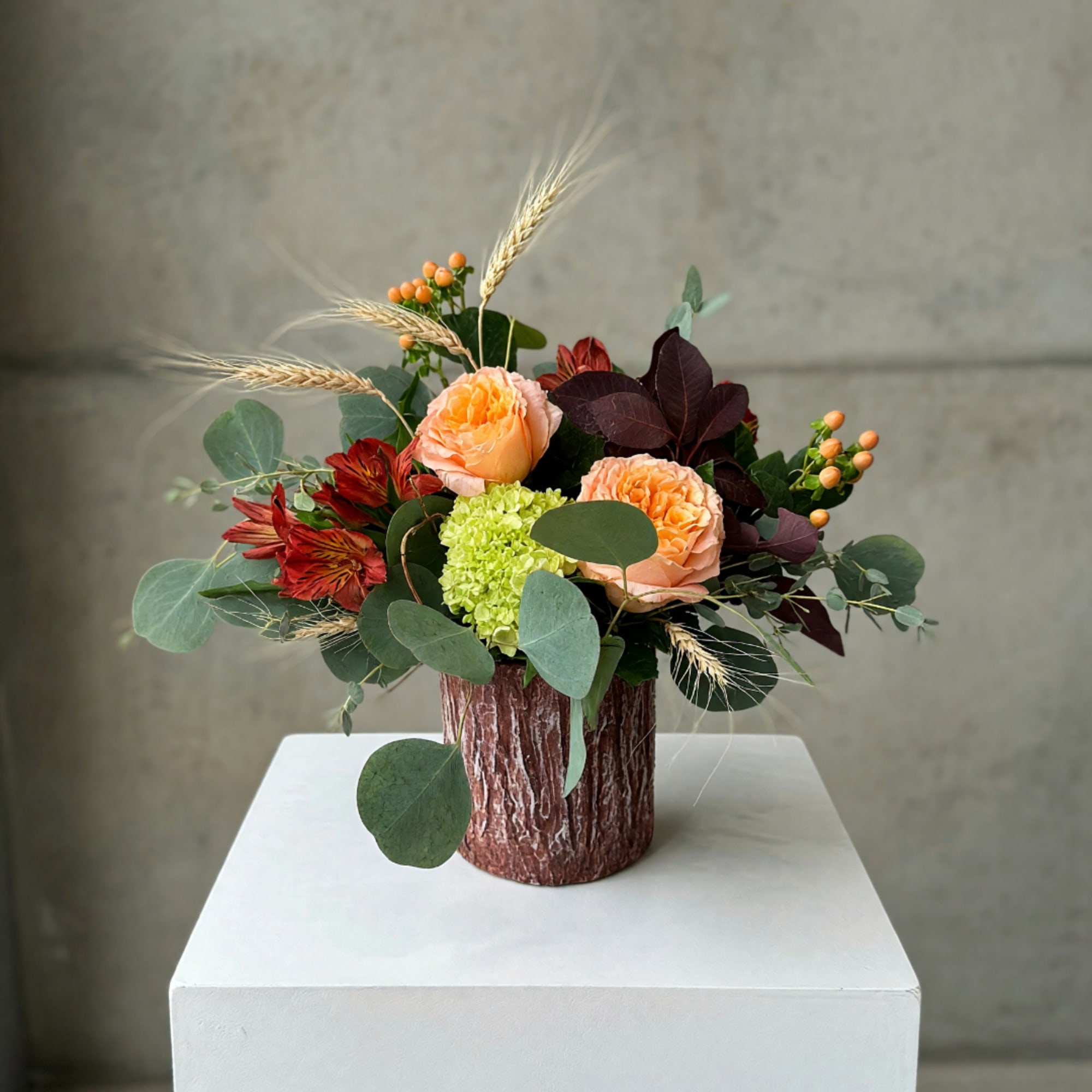 Peach roses and red flowers in a textured brown vase