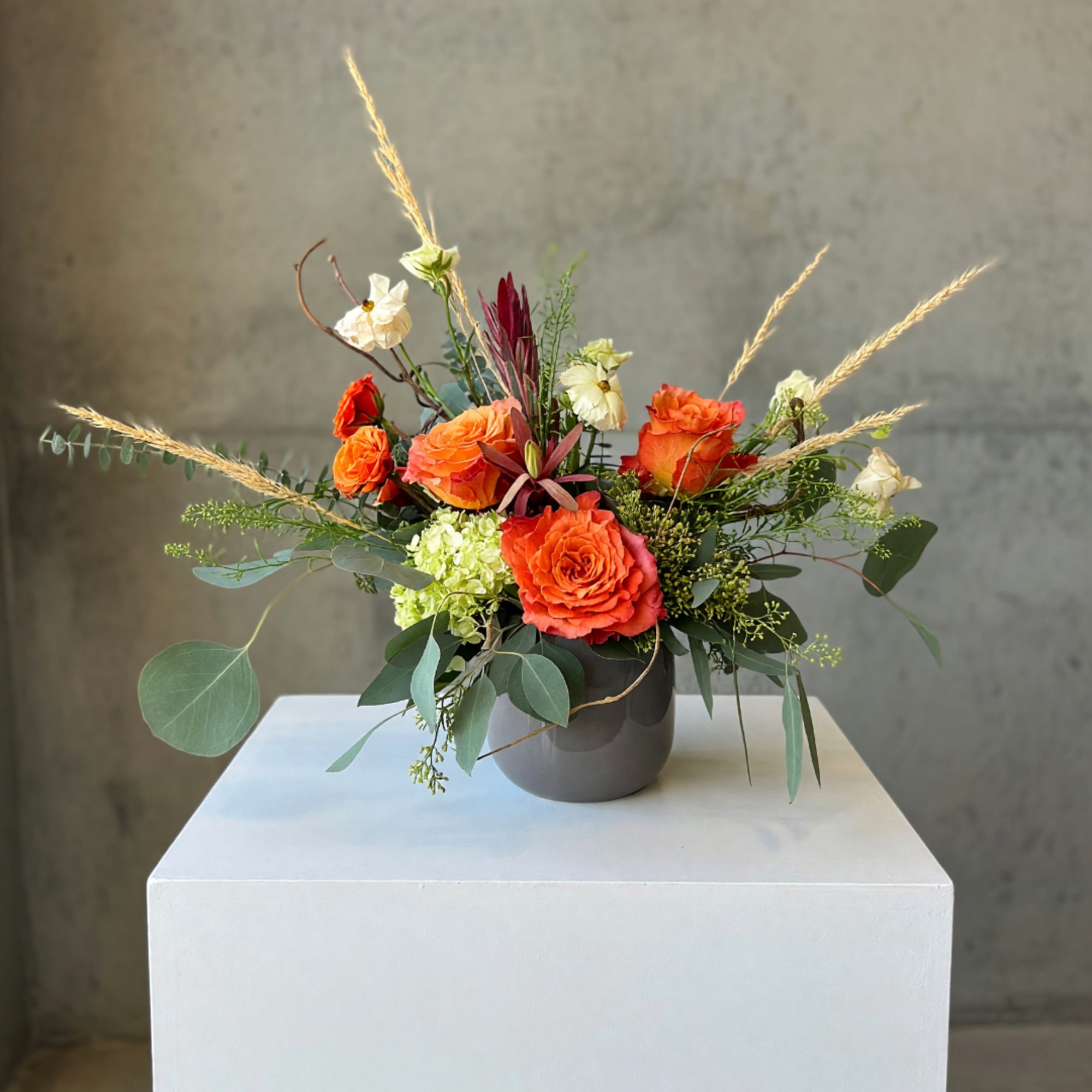 Orange roses and cream blooms in a gray vase with airy grasses