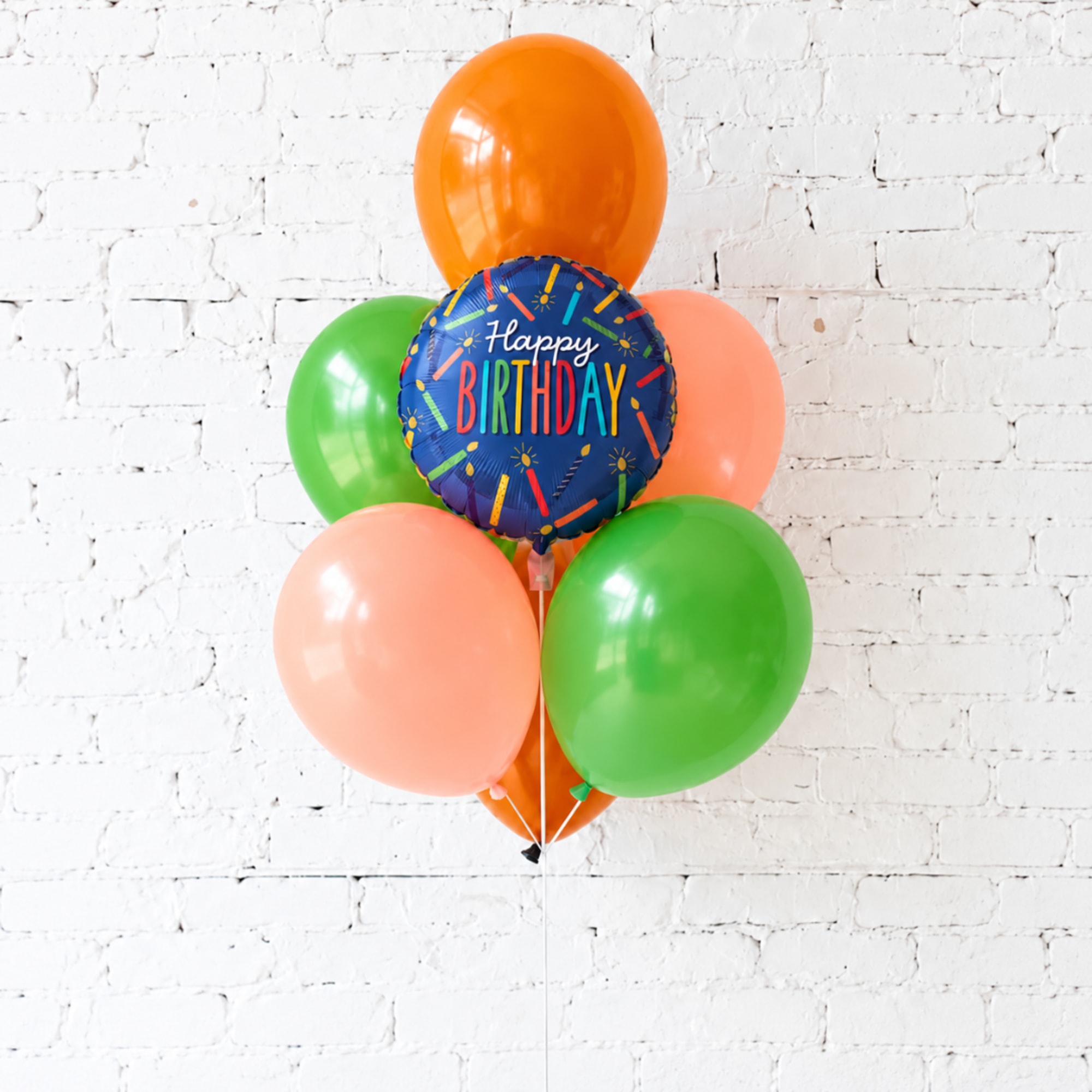 Cluster of colorful birthday balloons against a white brick wall