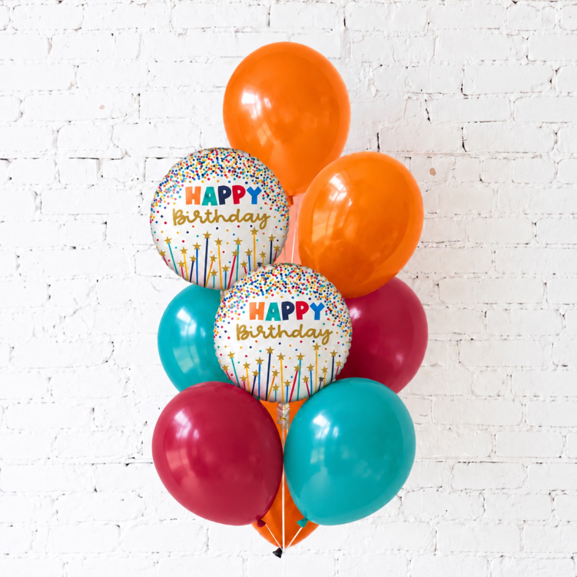 Cluster of colorful birthday balloons against a white brick wall