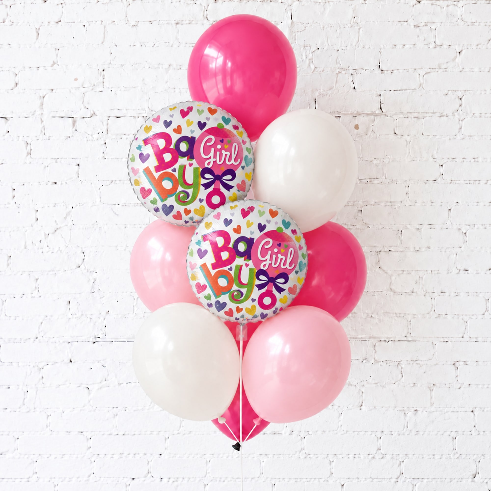 Pink and white baby girl balloons against a white brick wall