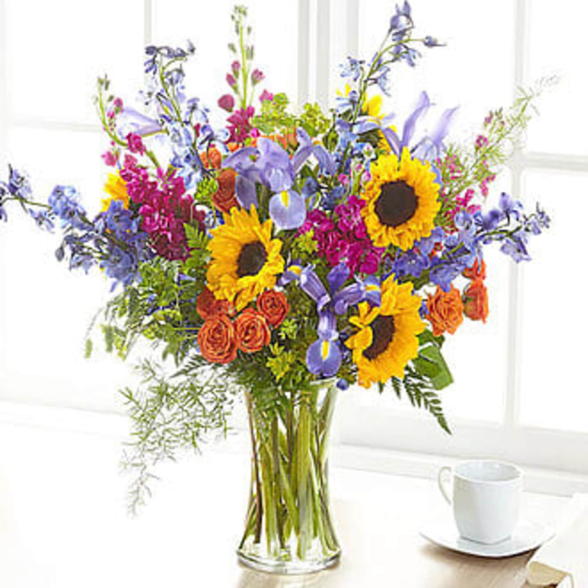 Mixed bouquet with sunflowers, irises, and orange roses in a glass vase