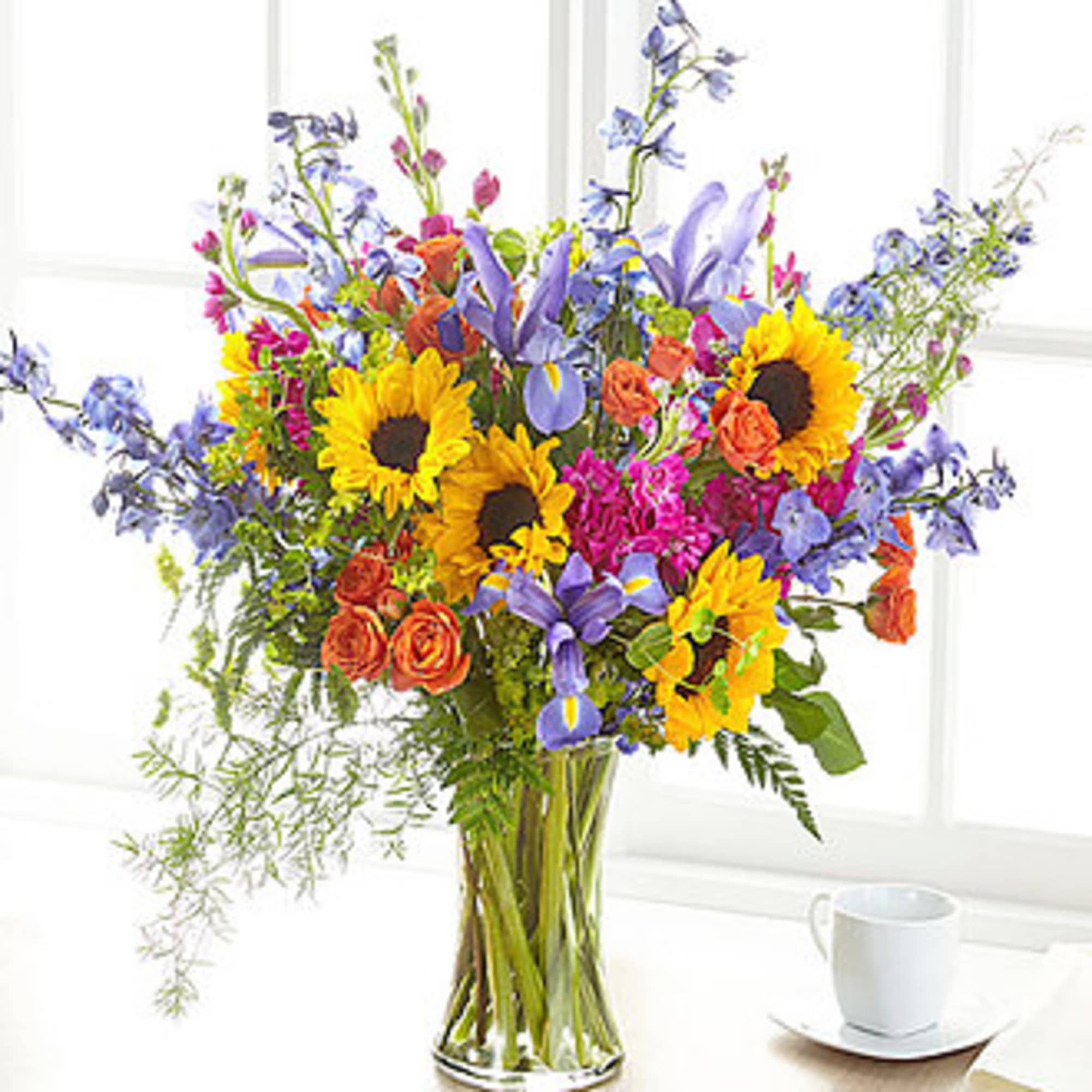 Mixed bouquet of sunflowers, roses, and purple flowers in a glass vase