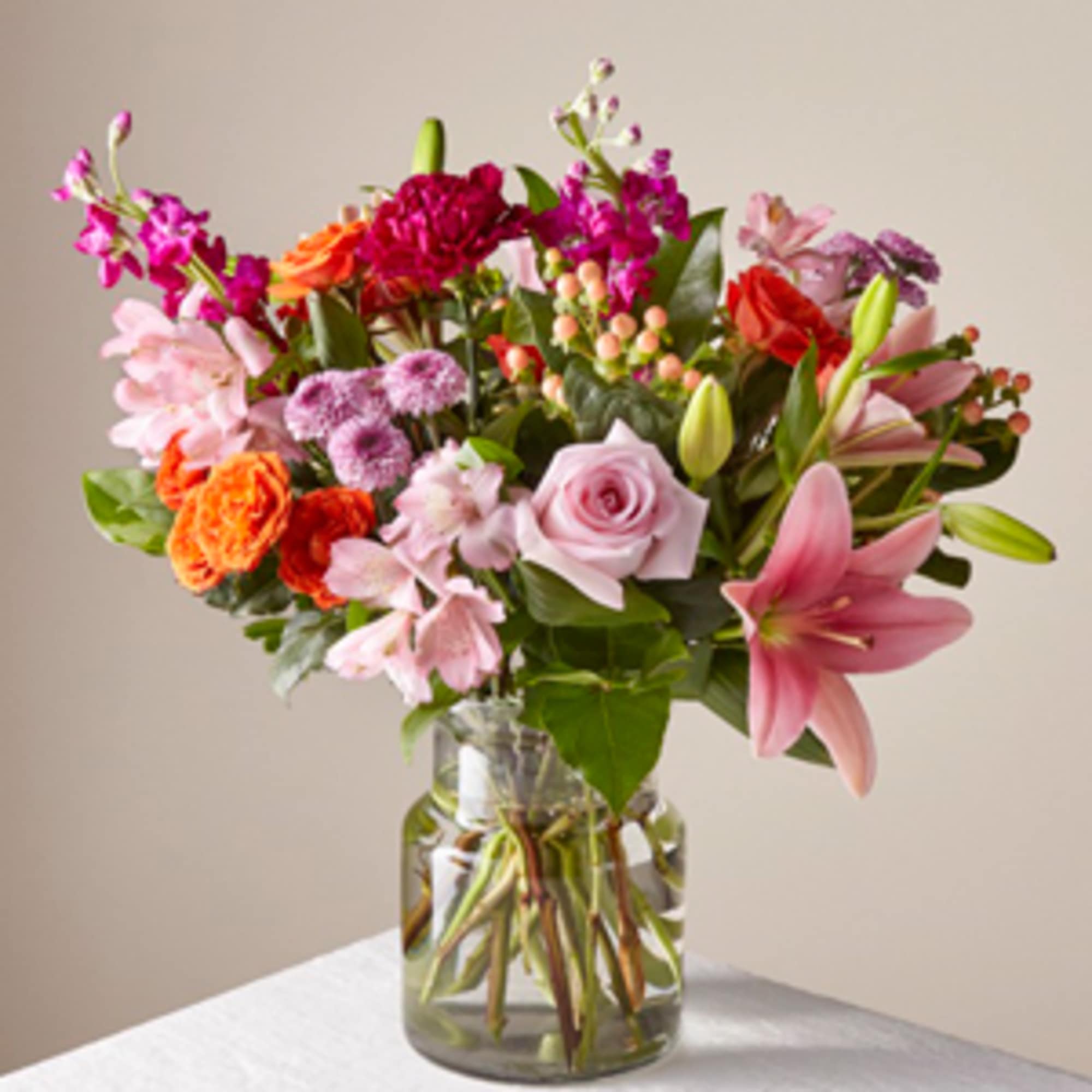 Mixed bouquet of pink, orange, and red flowers in a glass vase