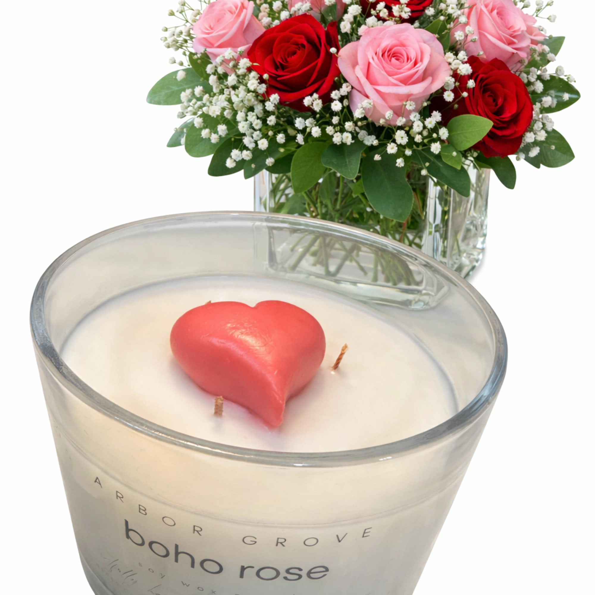 Pink and red roses in a glass vase beside a heart-shaped candle