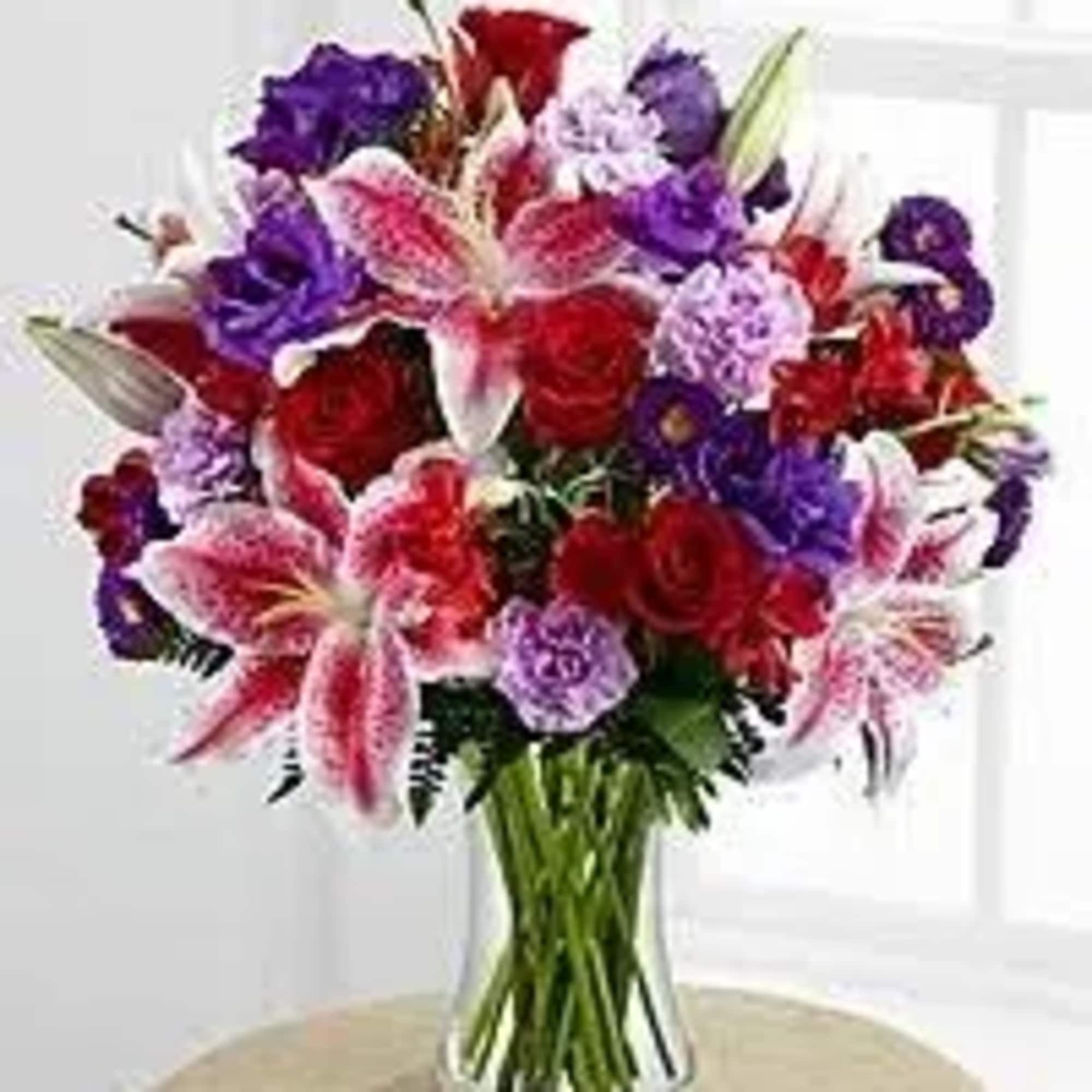 Tall bouquet of red roses, pink lilies, and purple flowers in a clear glass vase