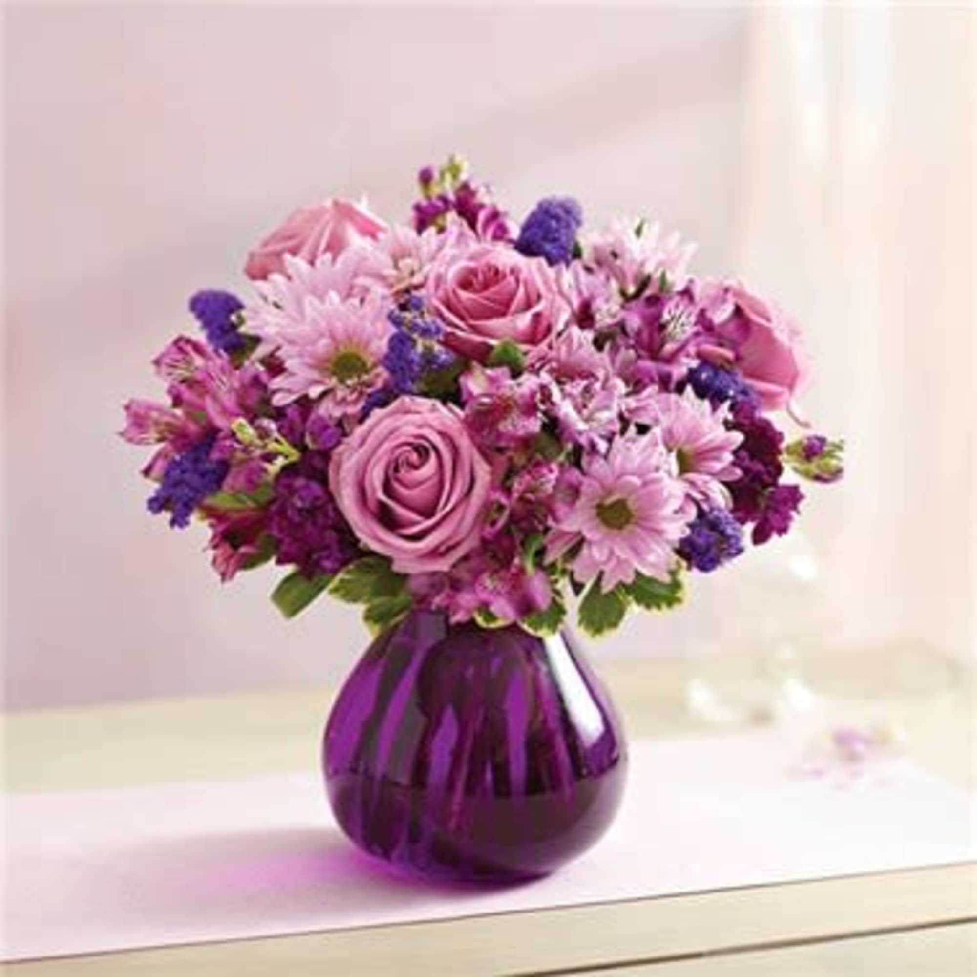 Pink and purple roses and daisies arranged in a round purple glass vase