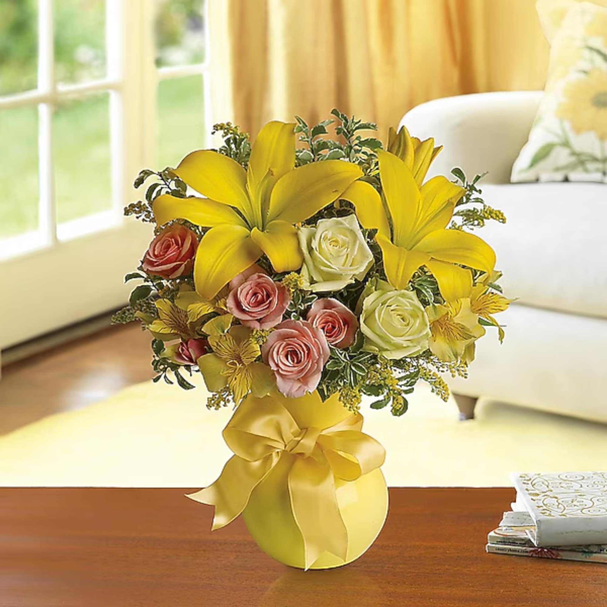 Yellow lilies and pink roses arranged in a vase with a satin bow
