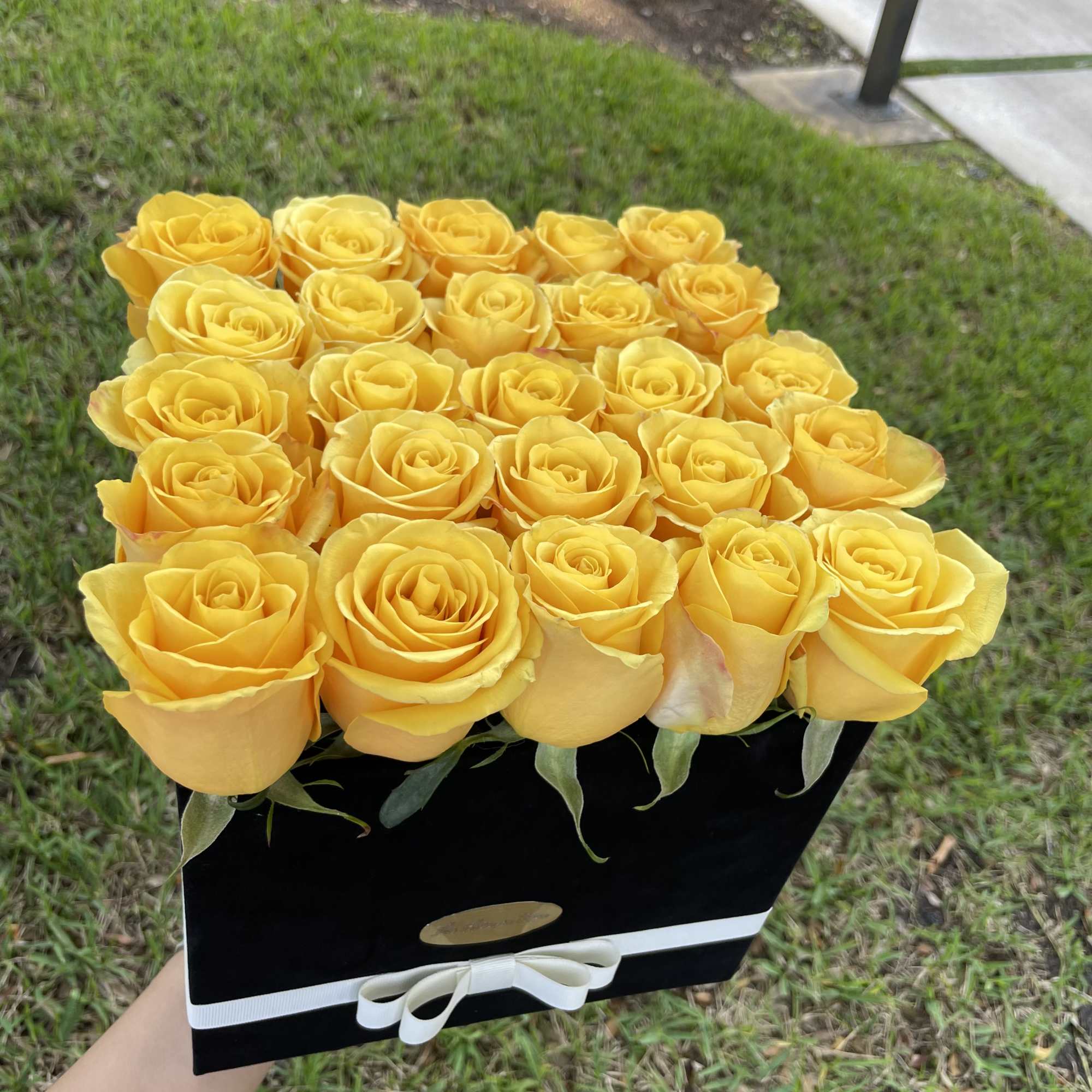 Bright yellow roses tightly packed in a black box with a white