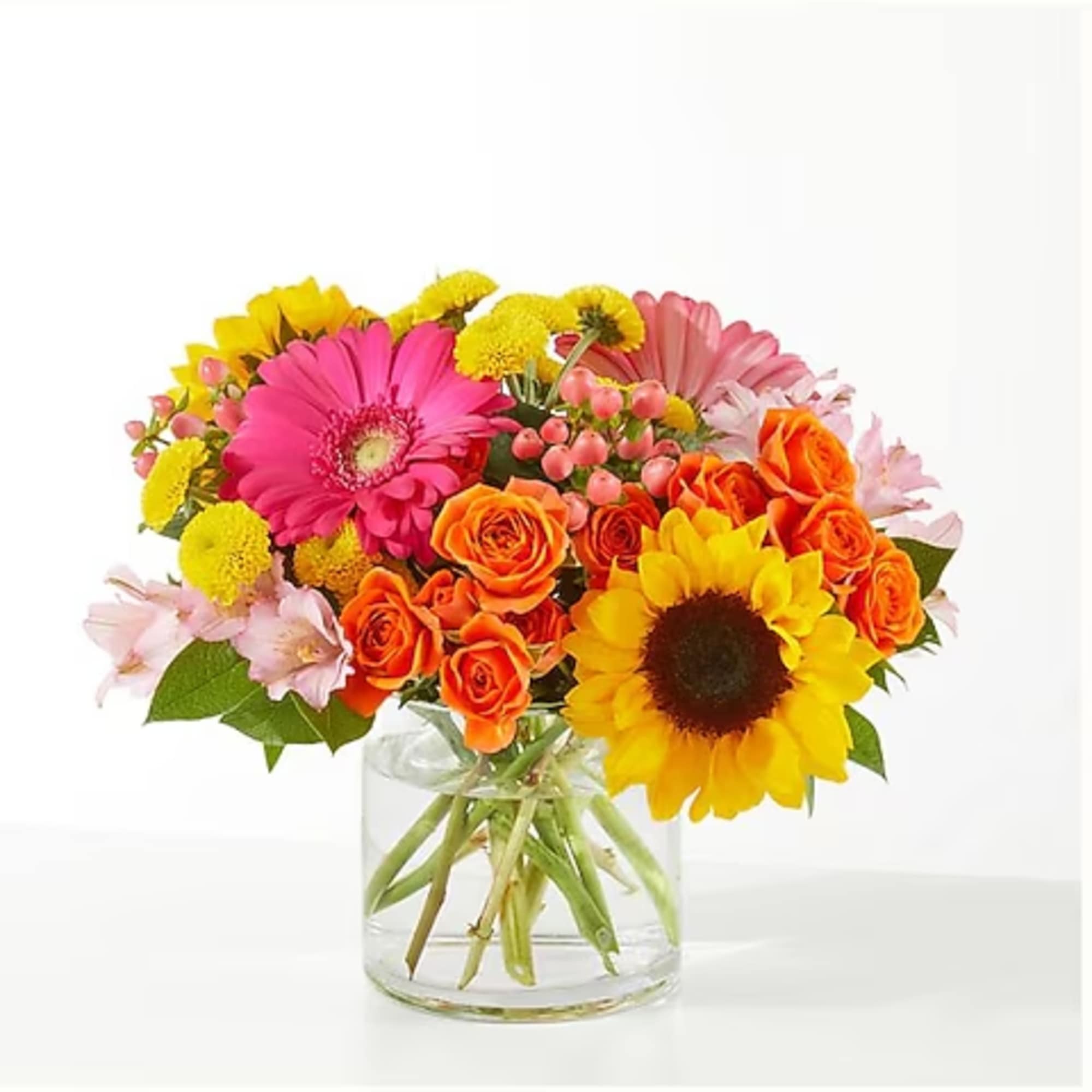Colorful bouquet of gerbera daisies, roses, and sunflowers in a clear glass vase