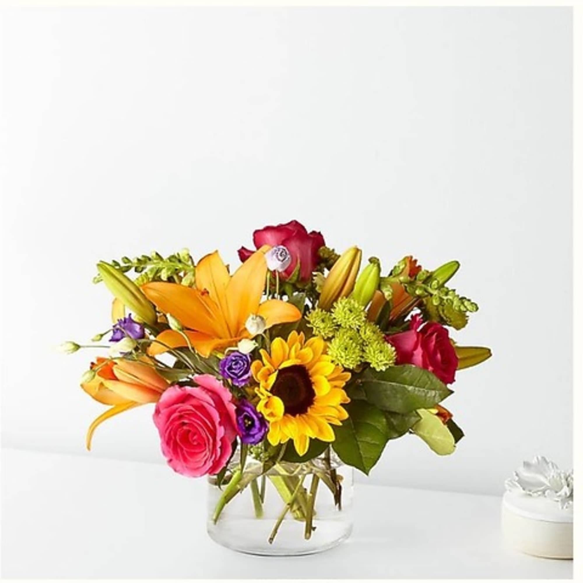 Mixed bouquet of roses, lilies, and a sunflower in a clear glass vase