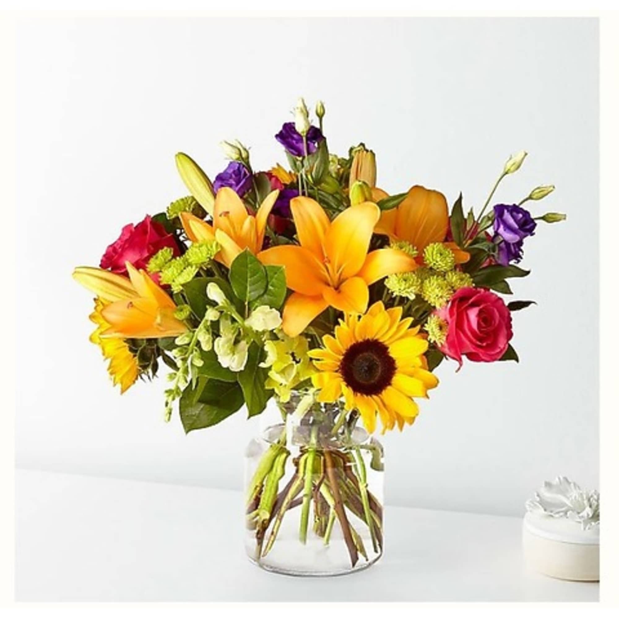 Mixed bouquet of orange lilies, pink roses, and a sunflower in a glass vase