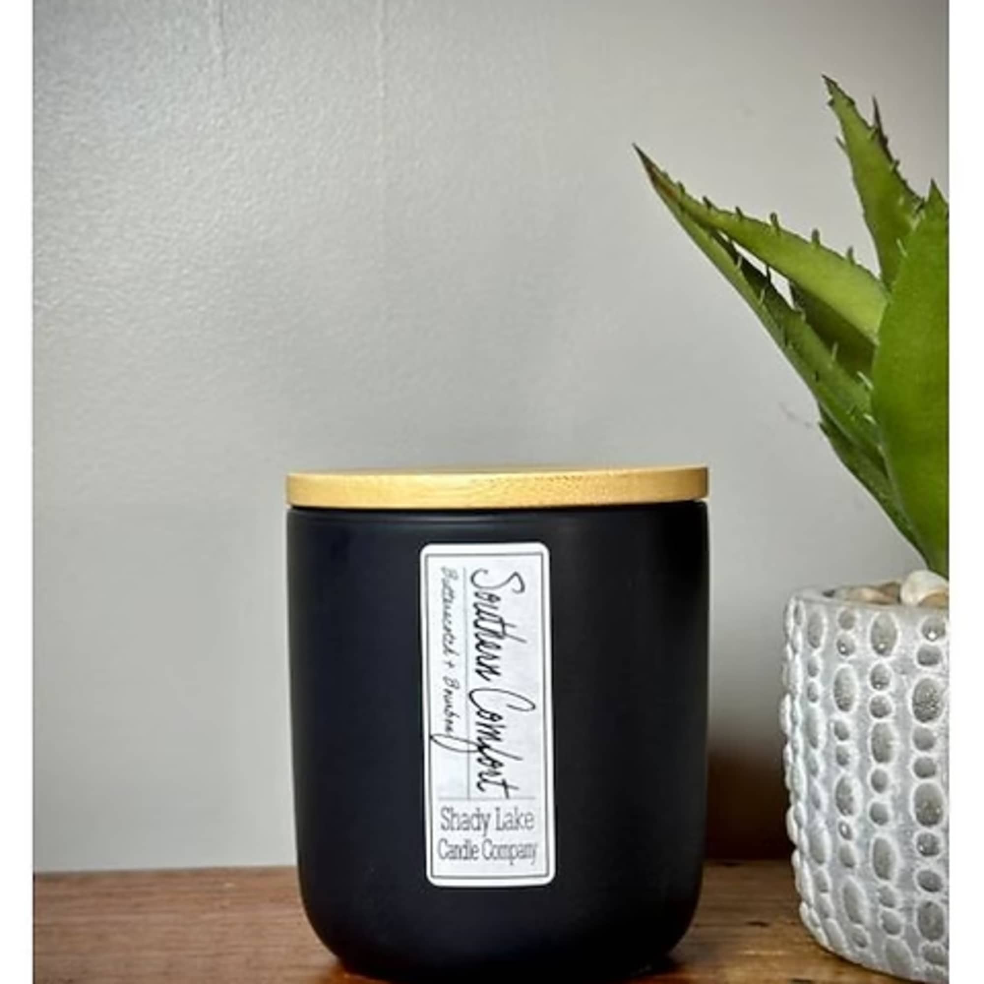 Black candle jar with a gold lid beside a small potted succulent