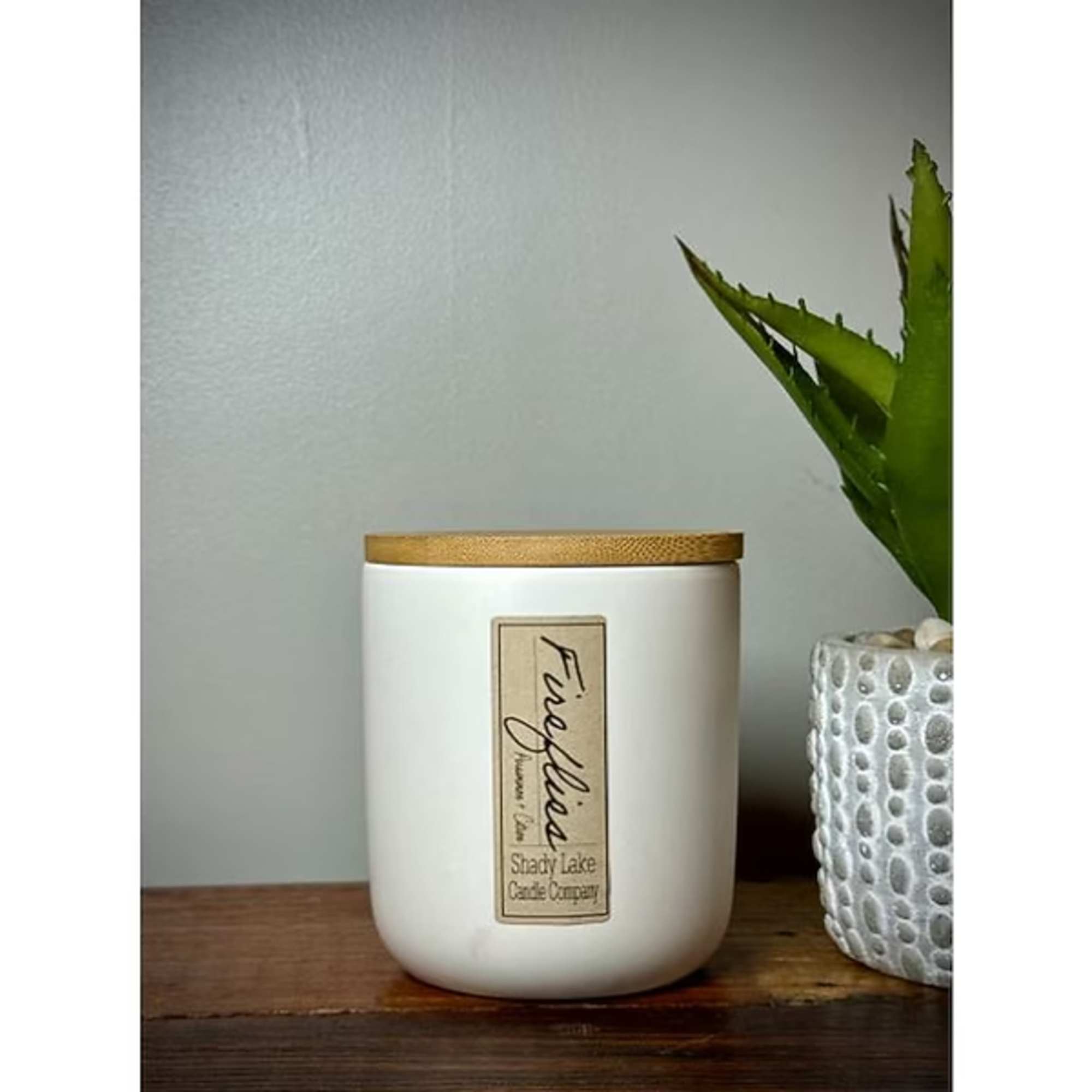 White candle jar with a wooden lid on a wooden surface