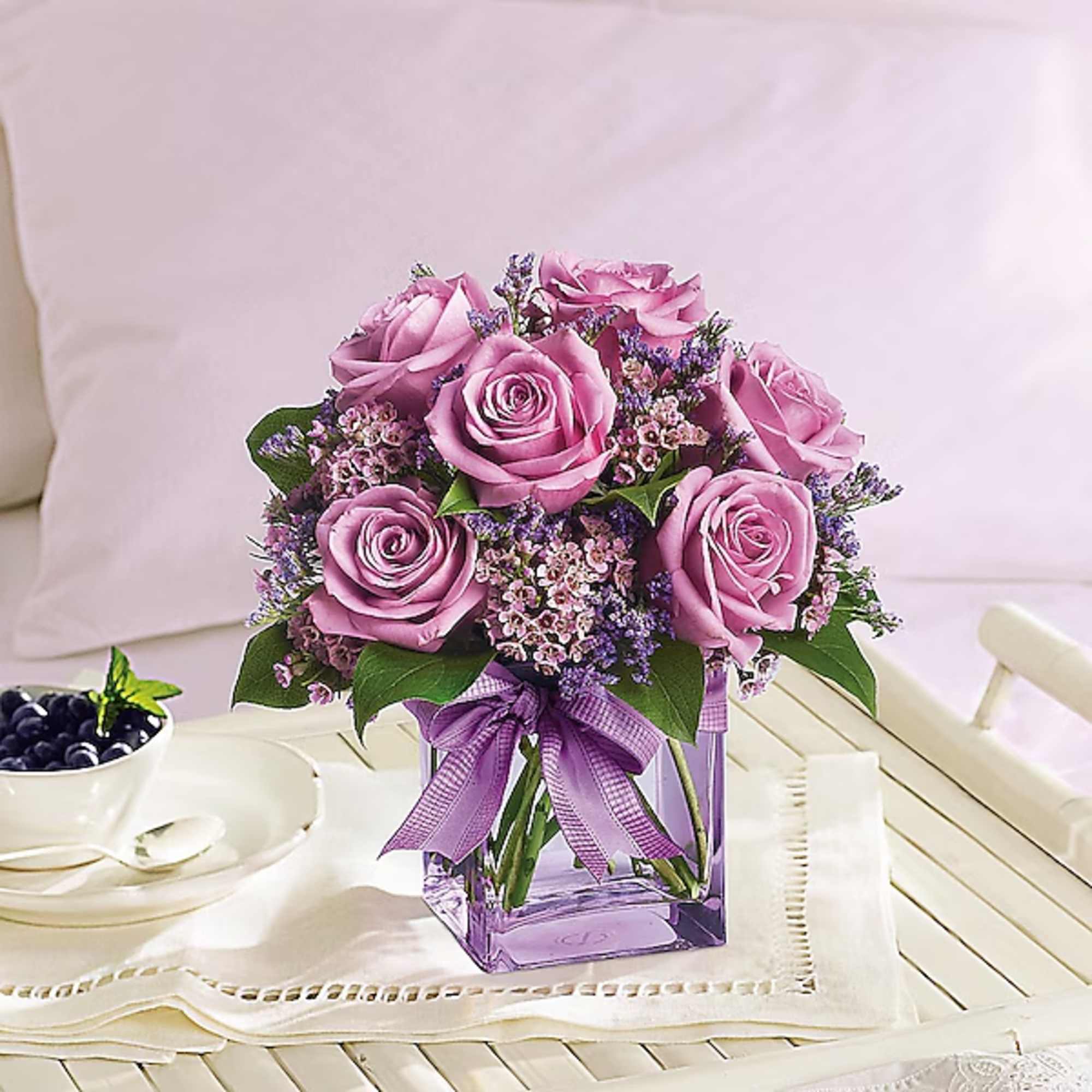 Pink roses in a purple glass vase with a ribbon bow