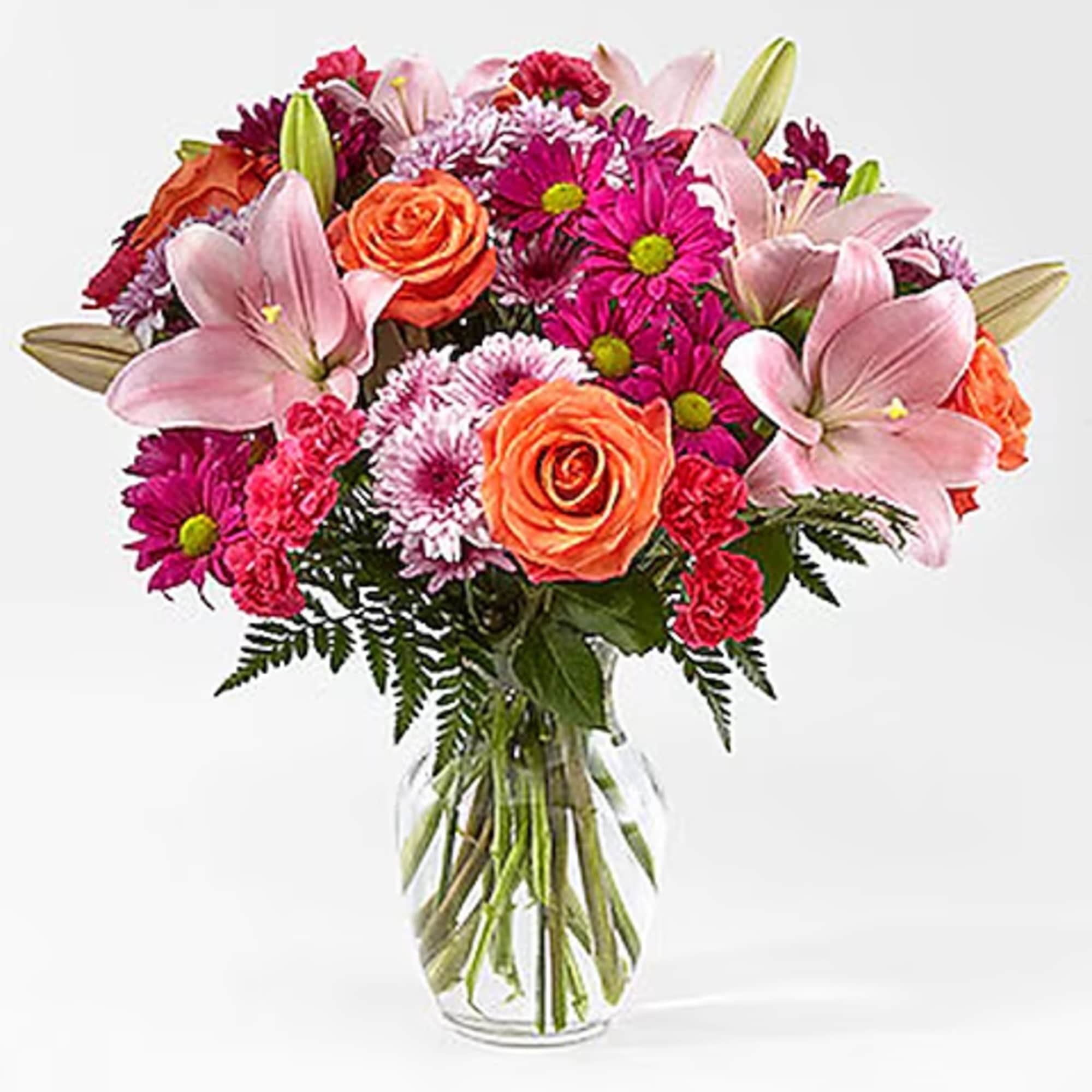 Mixed bouquet of pink lilies, orange roses, and magenta daisies in a glass vase