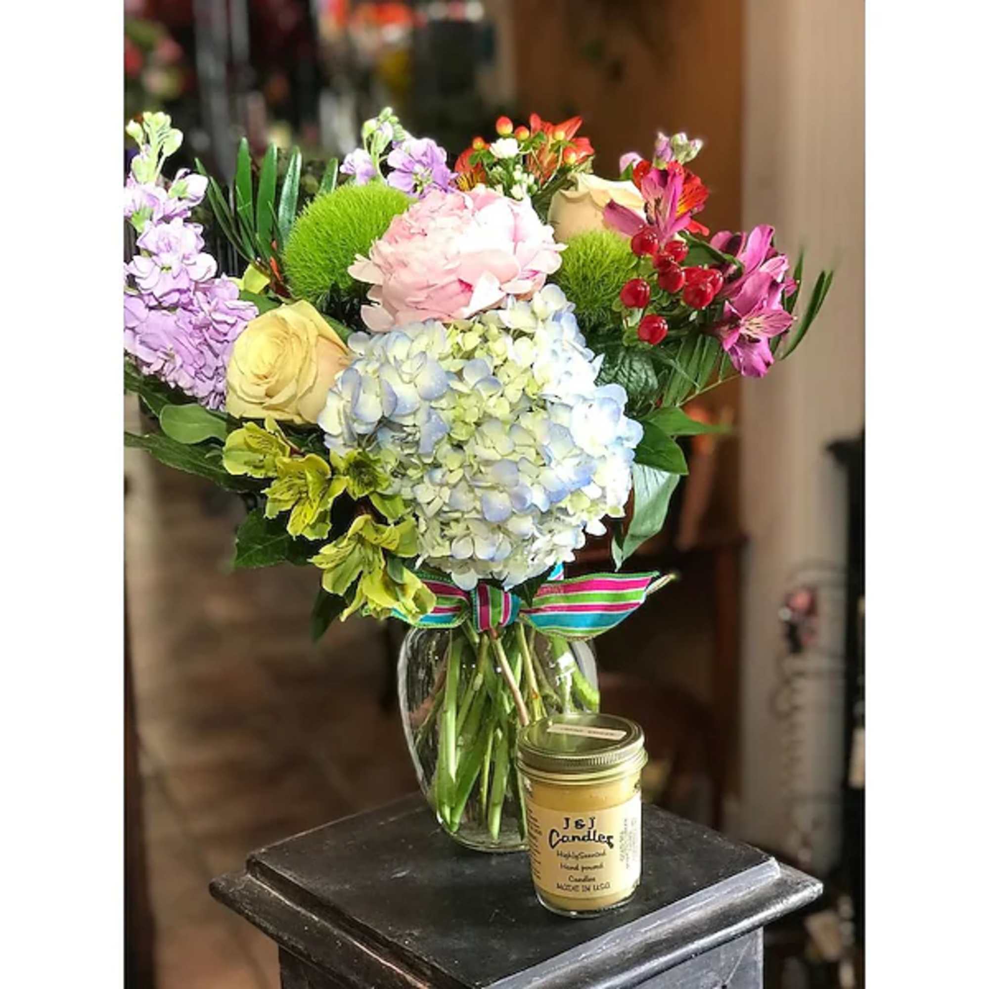 Mixed bouquet in a glass vase with a striped ribbon and a small candle jar
