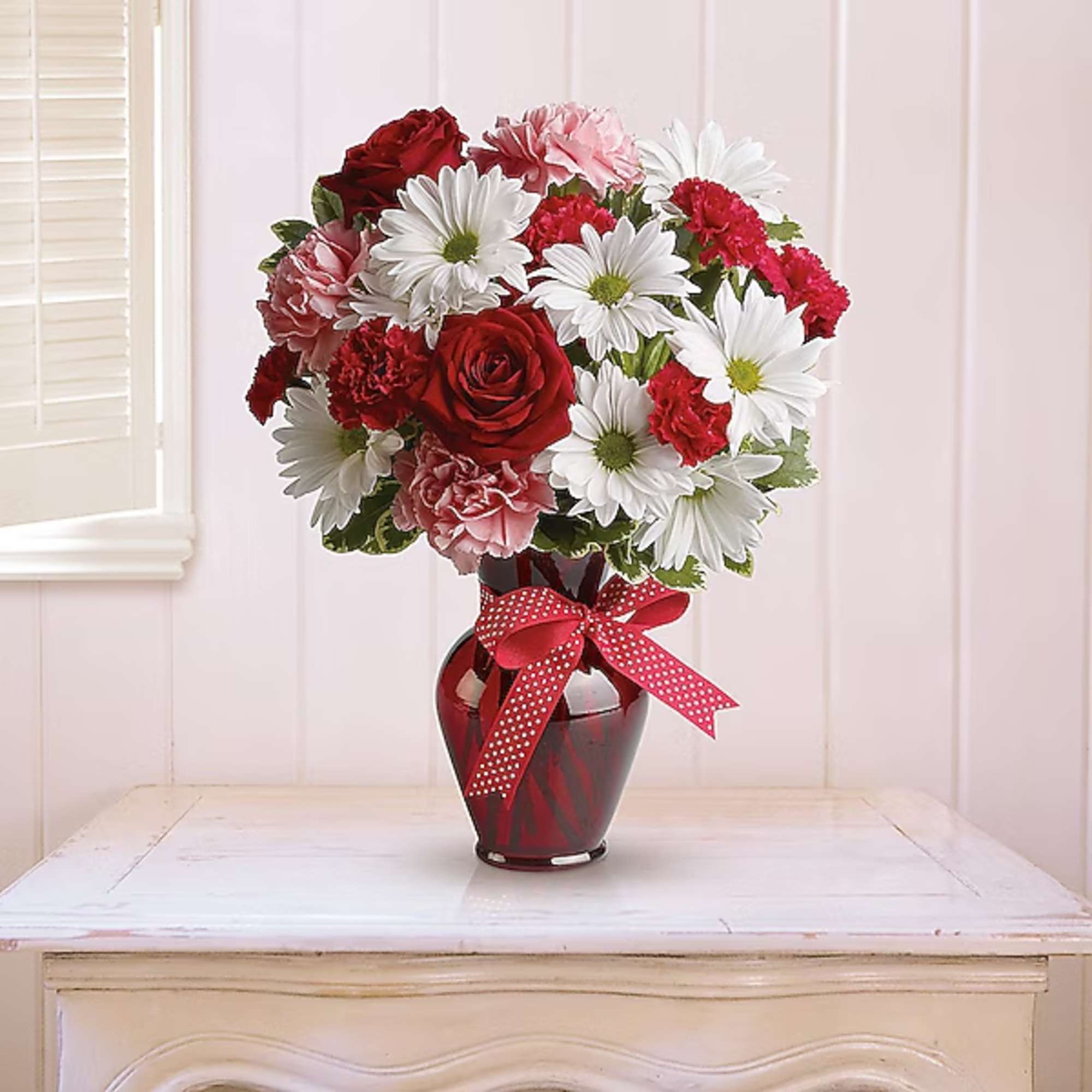 Bouquet of red roses, pink carnations, and white daisies in a red vase