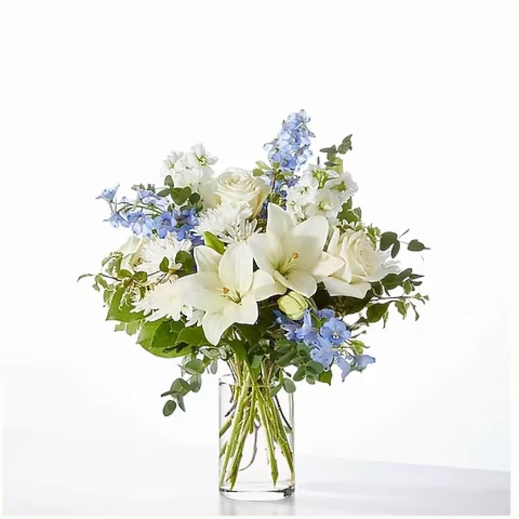 White lilies and roses with blue flowers in a clear glass vase