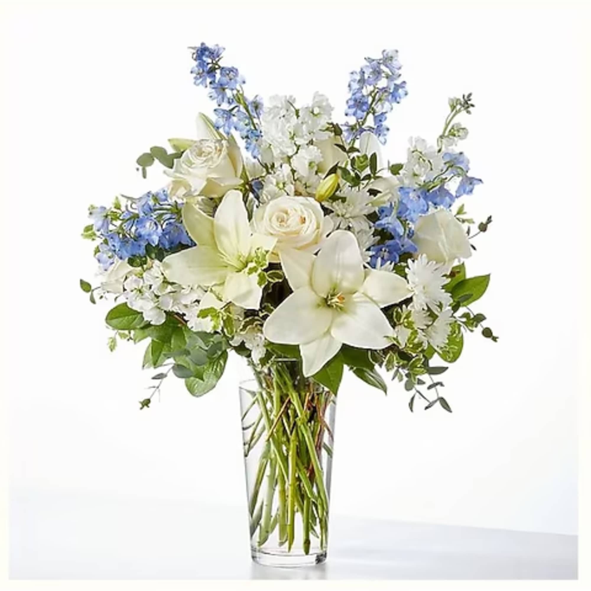 White lilies and roses in a clear glass vase with blue flowers