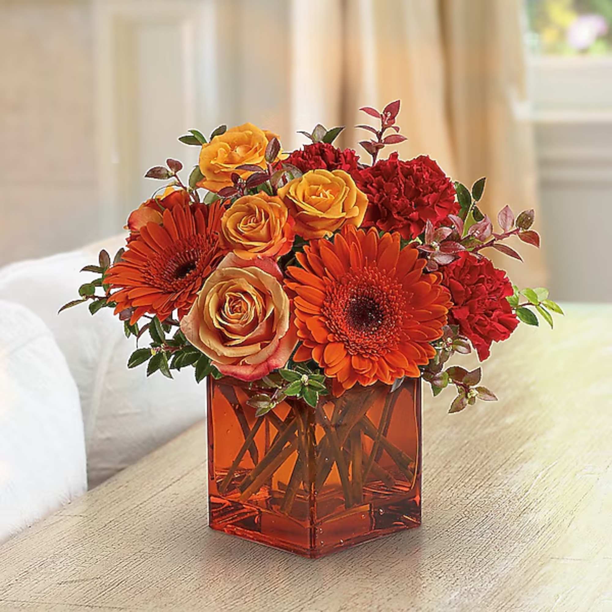 Orange and red flower arrangement in a square glass vase