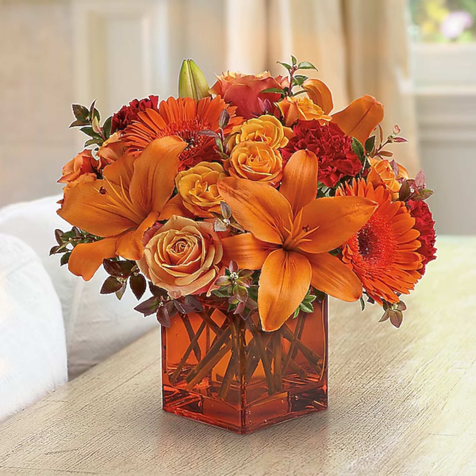 Orange and red flower arrangement in a square glass vase