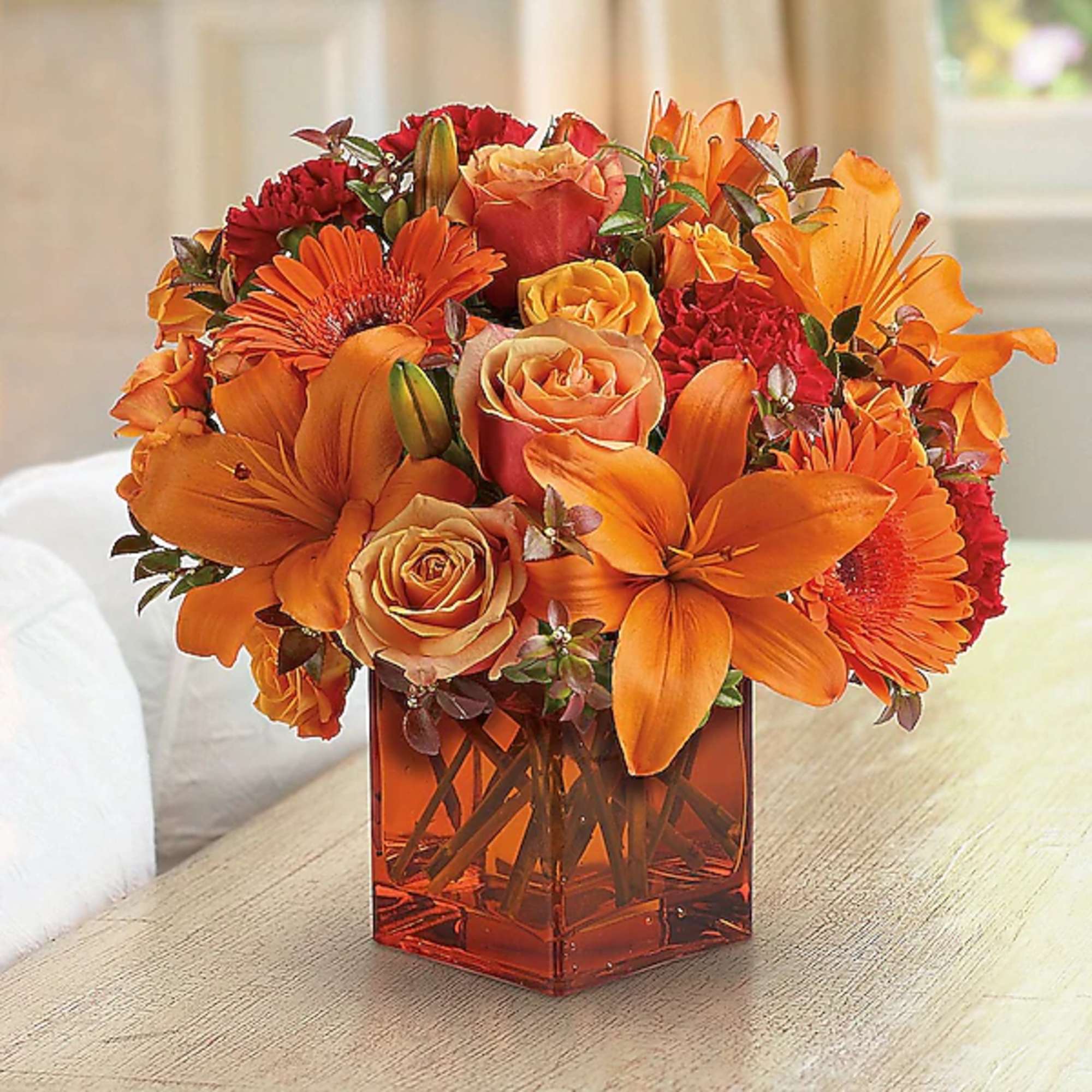 Orange and red flower arrangement in a square glass vase