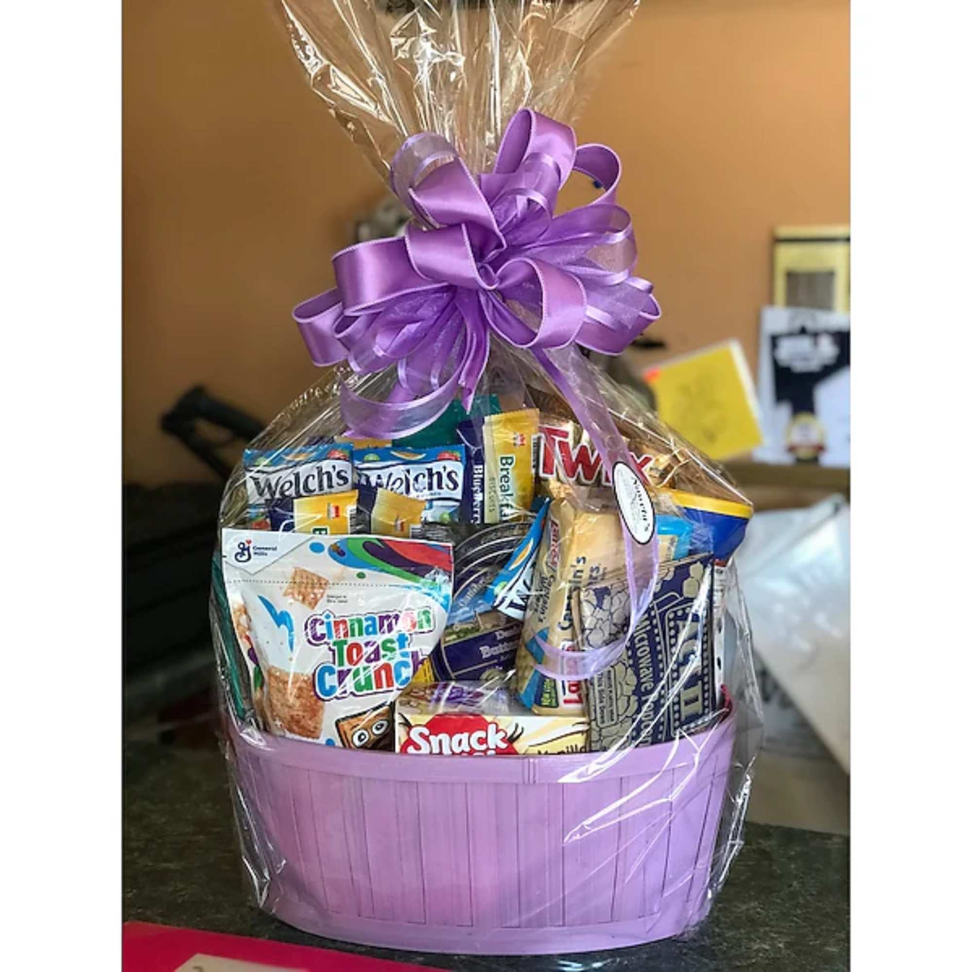 Gift basket of assorted snacks in a lavender basket with a purple bow