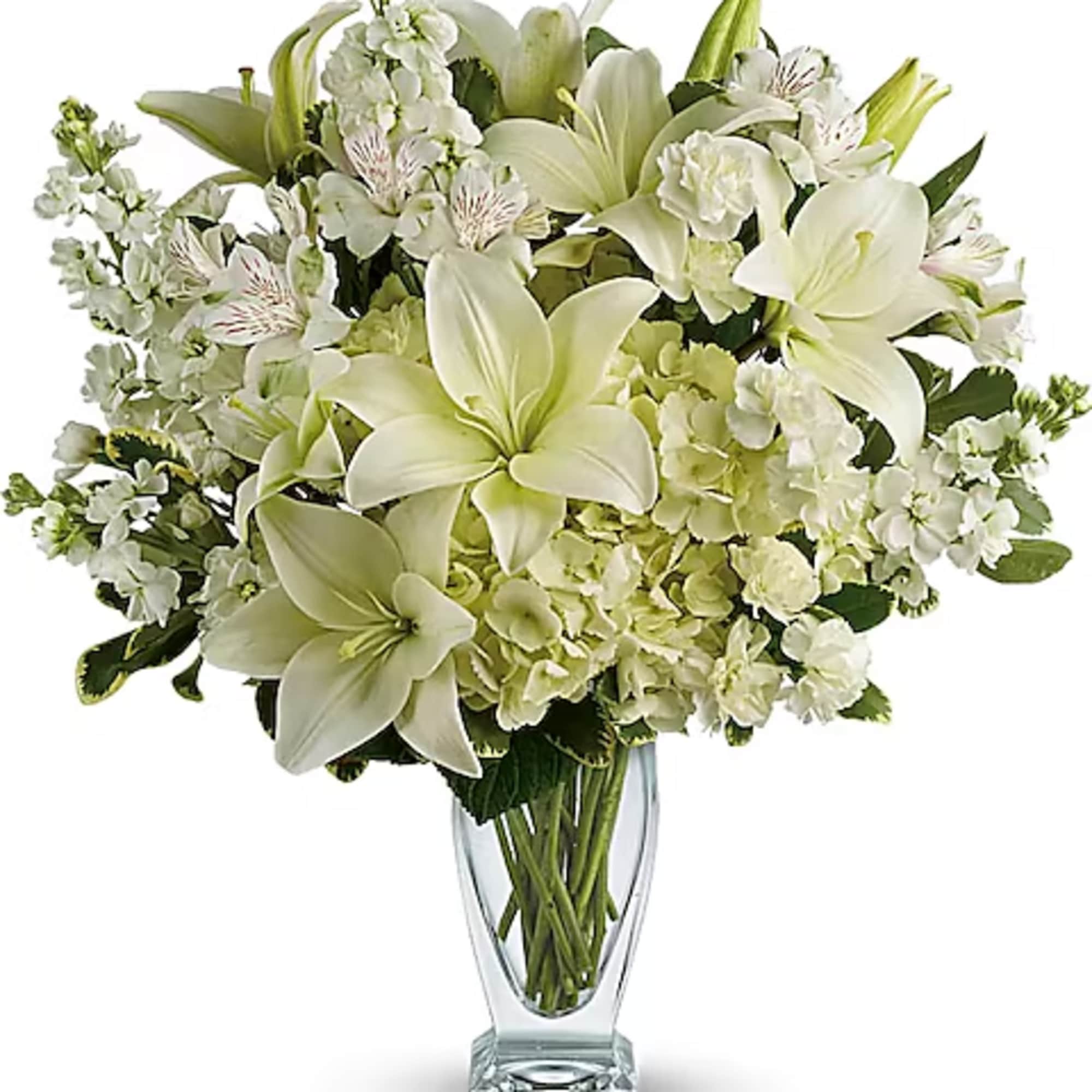 White lilies and mixed white flowers arranged in a clear glass vase