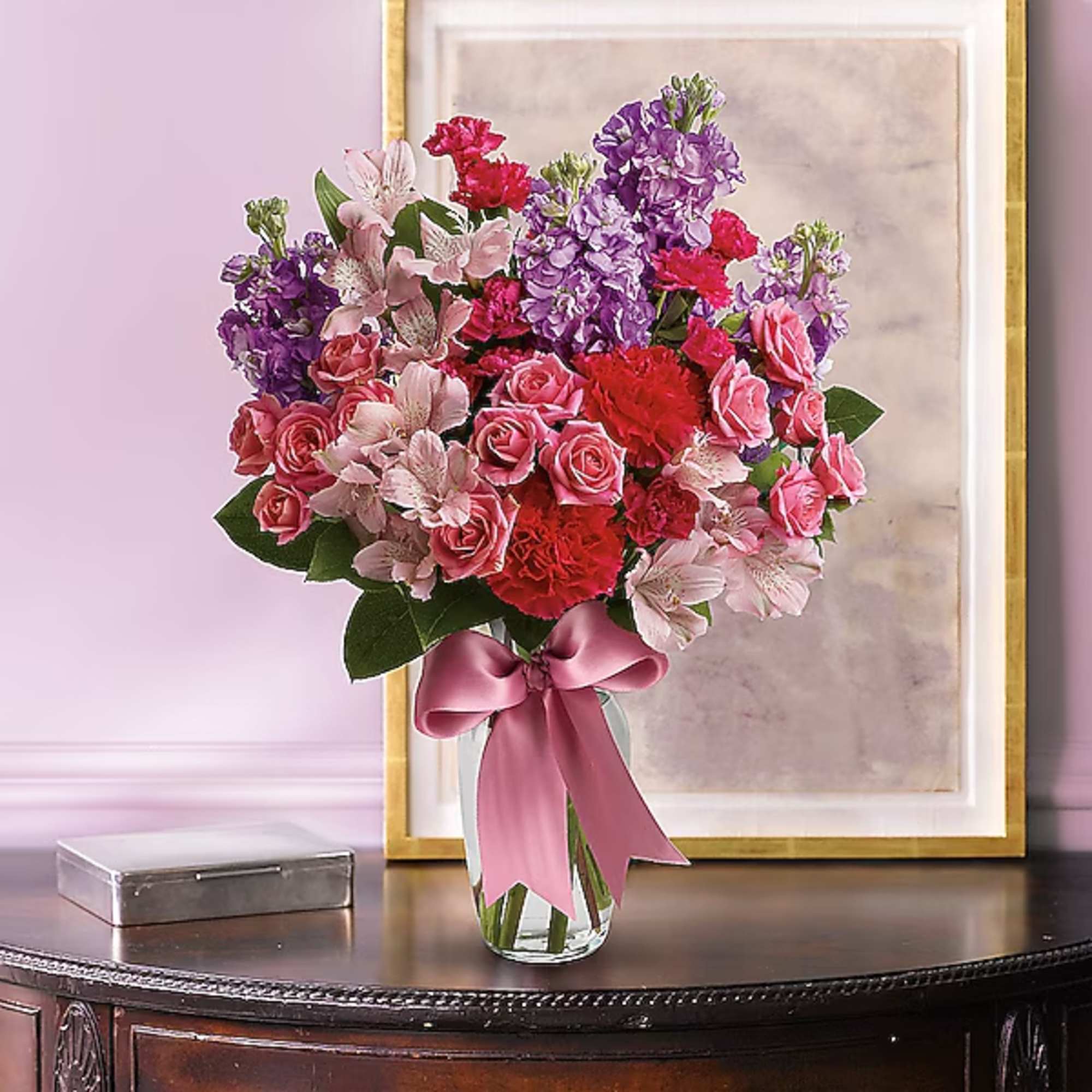 Pink and purple mixed bouquet in a clear glass vase with a satin ribbon