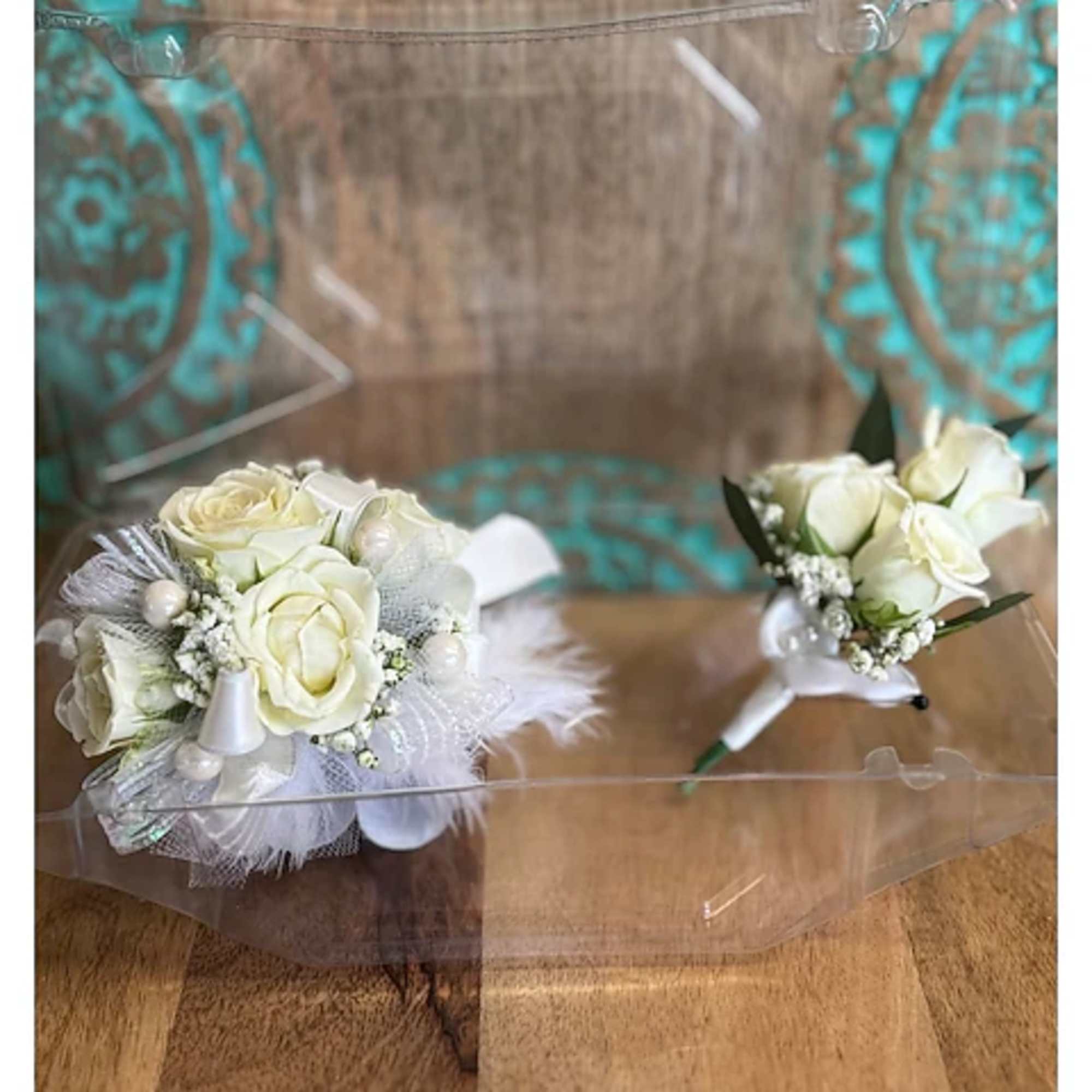Two small white rose boutonnieres with feather accents