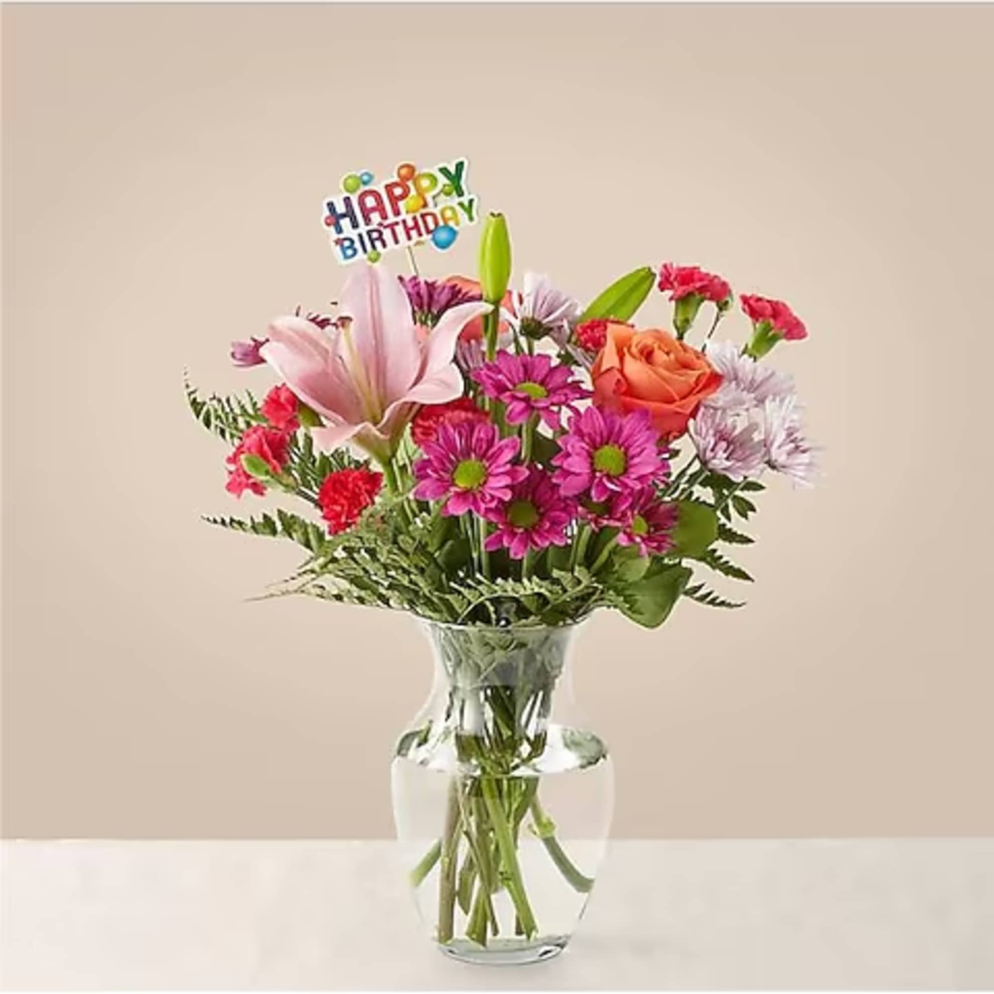Mixed bouquet in a clear glass vase with a birthday pick