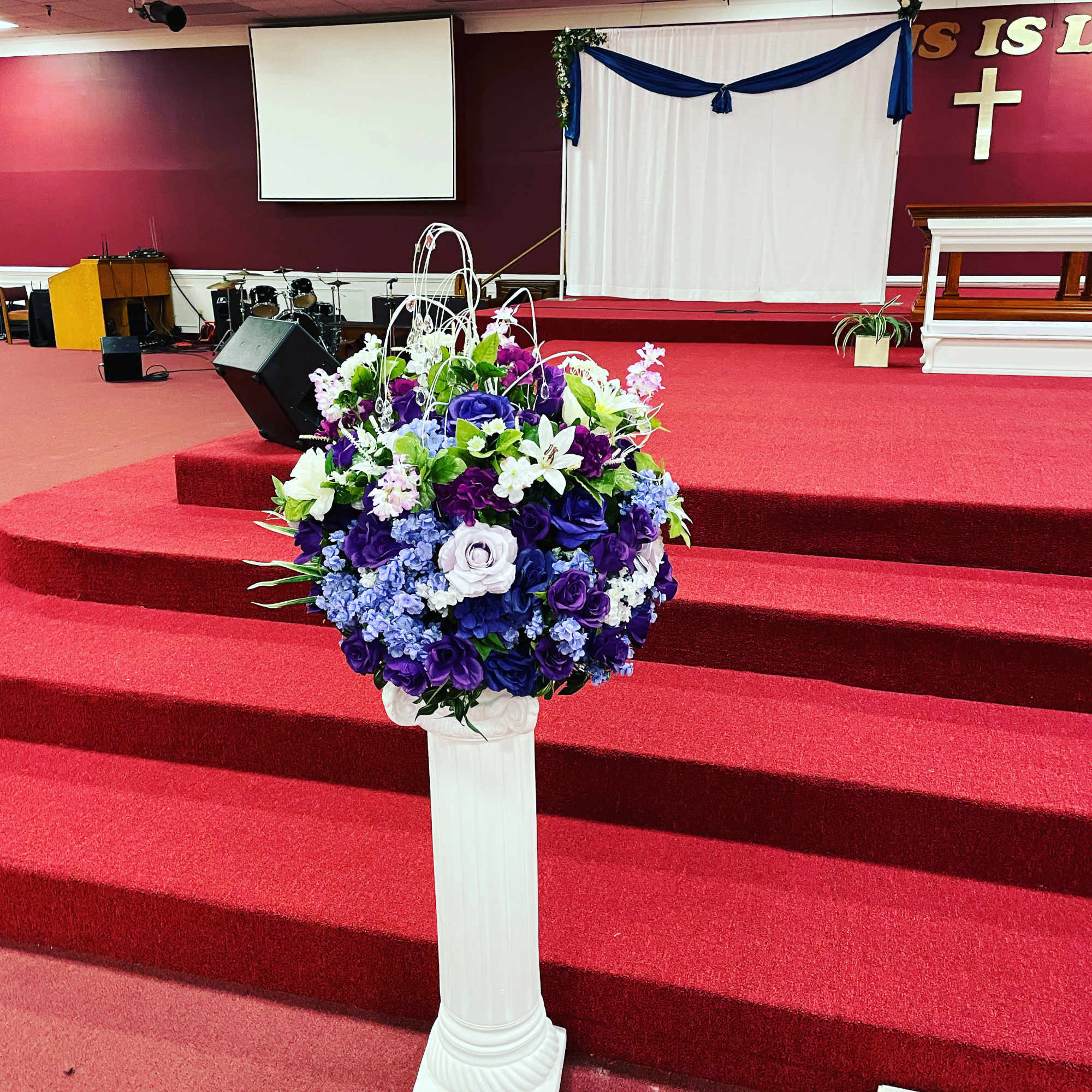 Purple and white floral arrangement on a white pedestal in a church sanctuary