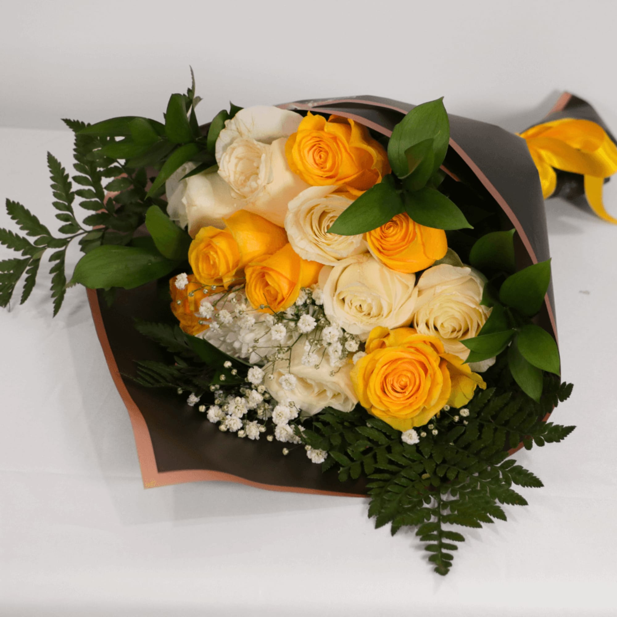 Bouquet of yellow and cream roses with fern foliage in dark wrap