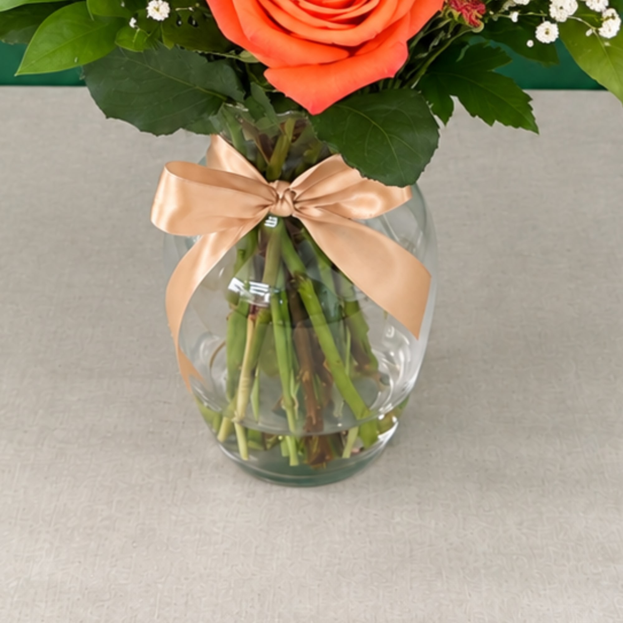 Orange rose arrangement in a clear glass vase with a satin bow