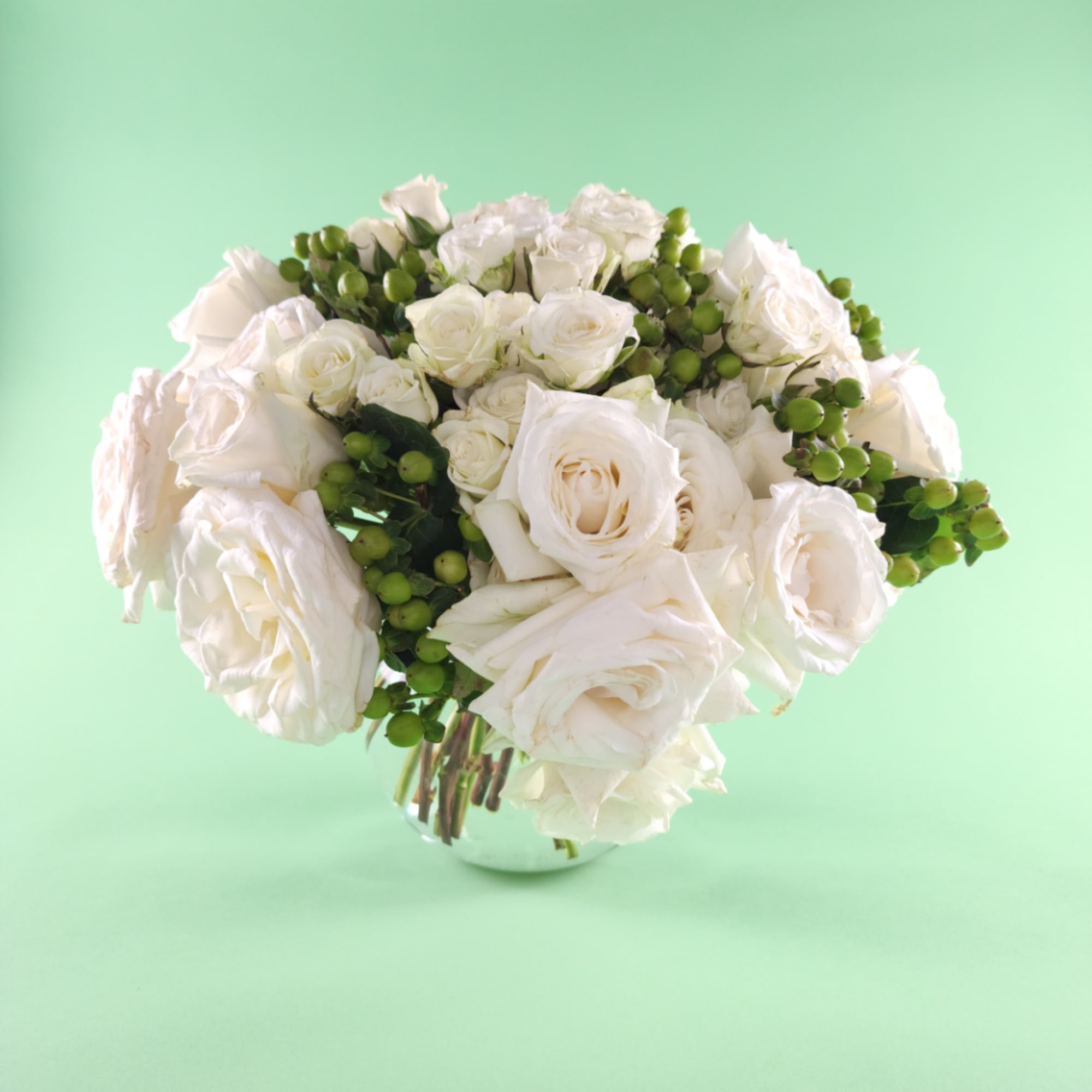 White rose bouquet with green berry accents in a clear vase