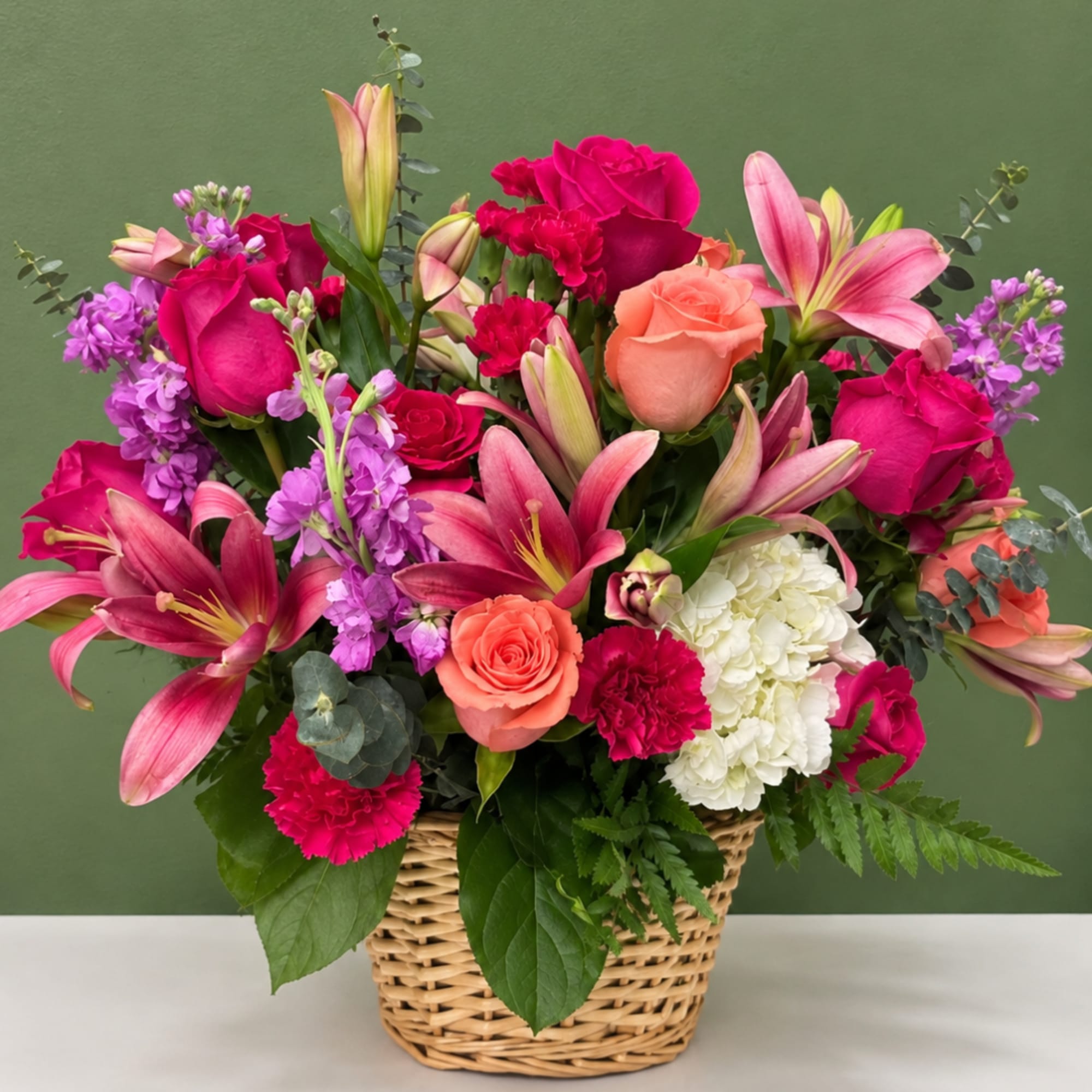 Mixed bouquet in a wicker basket with roses, lilies, carnations, and hydrangea